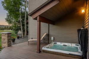 Outdoor deck featuring a hot tub, covered patio area, and stone-clad column