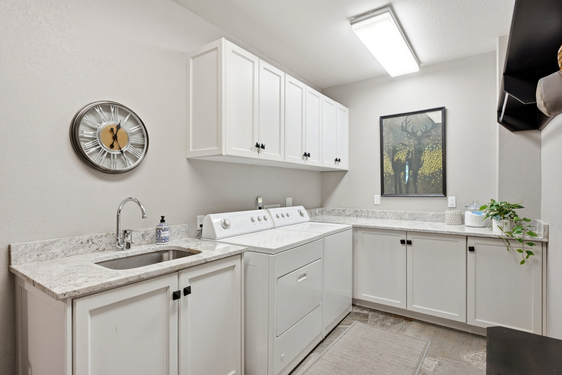 Laundry room with extensive white cabinetry, light-toned countertops, and a utility sink with a chrome faucet