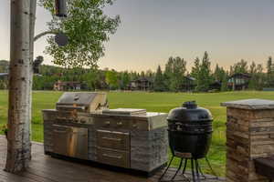 Outdoor cooking station featuring a stainless steel built-in grill, stone-clad base, and a separate ceramic smoker