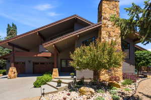 Modern exterior featuring a stone chimney, wood-finish garage doors, concrete steps, and a landscaped rock garden