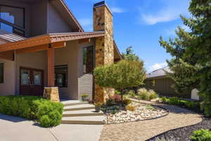Modern exterior featuring a stone chimney, wood beams, and double entry doors