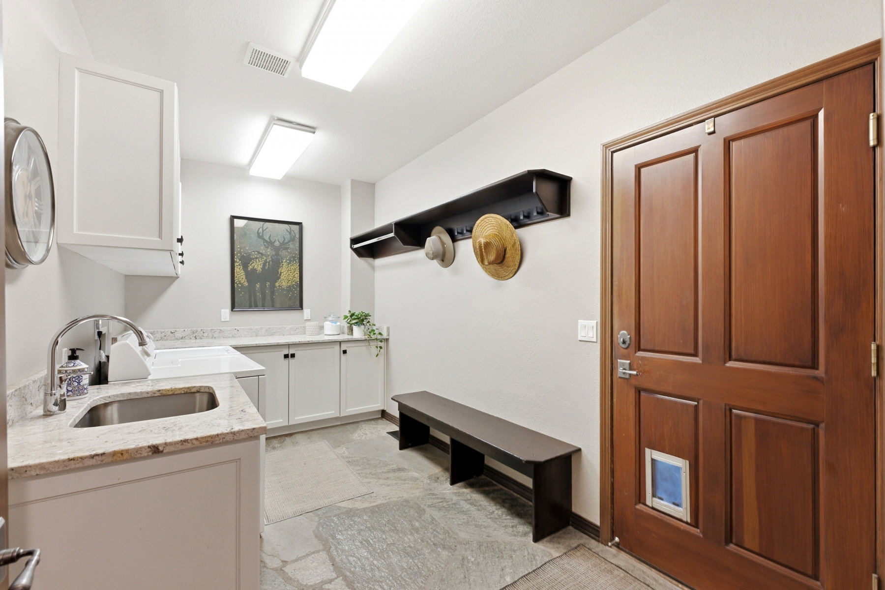 Utility room featuring a stainless steel sink, granite countertops, white cabinetry, slate tile flooring, and a wood-paneled door