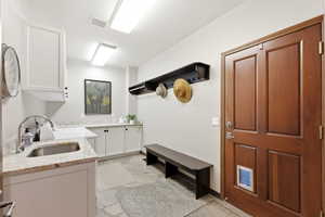 Utility room featuring a stainless steel sink, granite countertops, white cabinetry, slate tile flooring, and a wood-paneled door