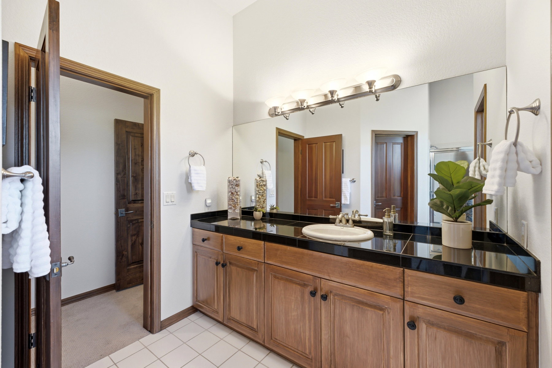 Vanity featuring wood cabinetry with black hardware, a black tile countertop, and an oval undermount sink with a chrome faucet