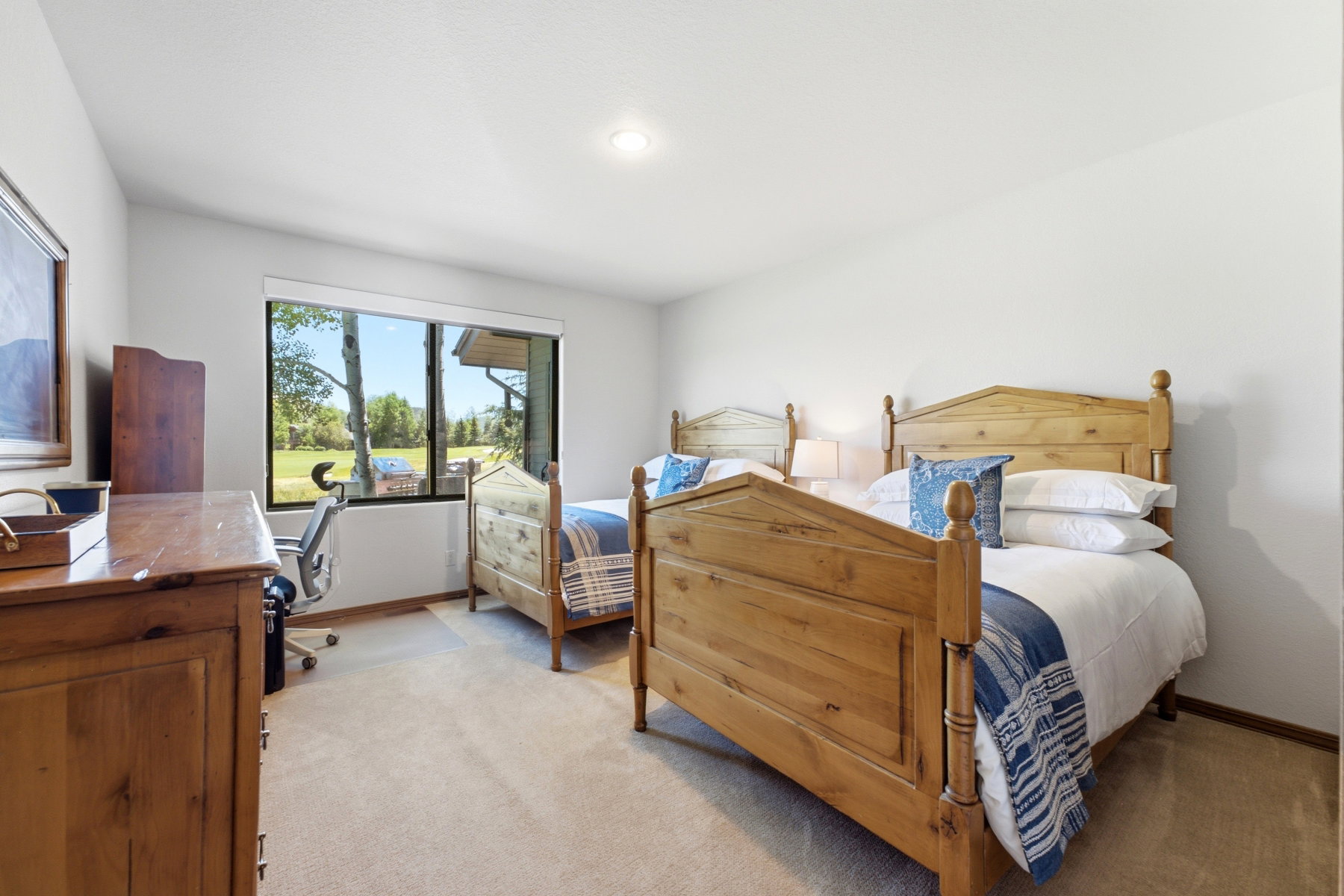 Carpeted room with two wooden bed frames, a large window, and a light-colored wall