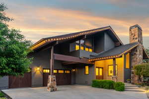 Modern architectural dwelling featuring a stone chimney, extensive window placement, a covered entry, and a two-car garage with wood-finish doors