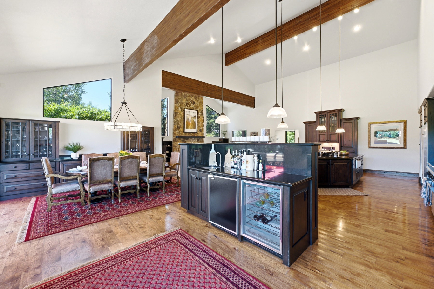 Vaulted ceilings with exposed wood beams, wood-finish flooring, and a stone-clad fireplace