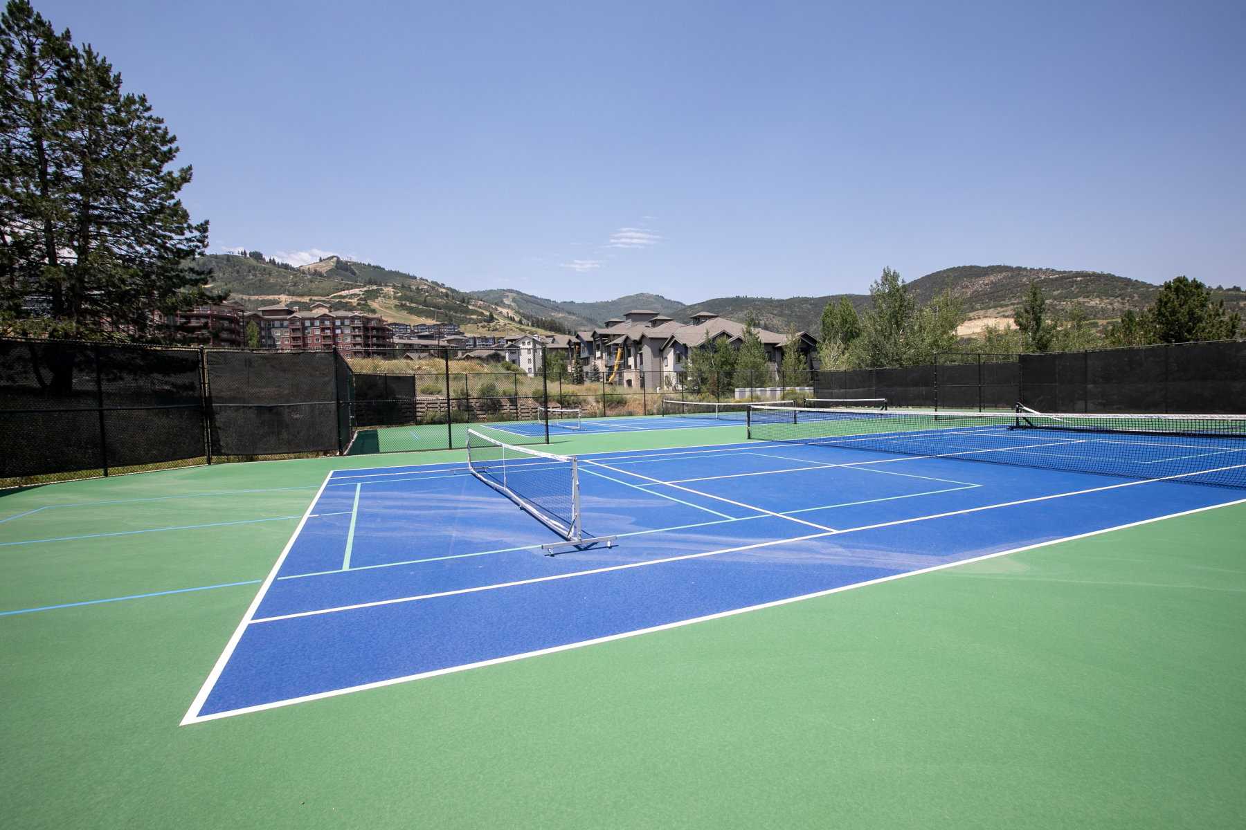 Two hard tennis courts featuring vibrant blue playing surfaces and green surrounds