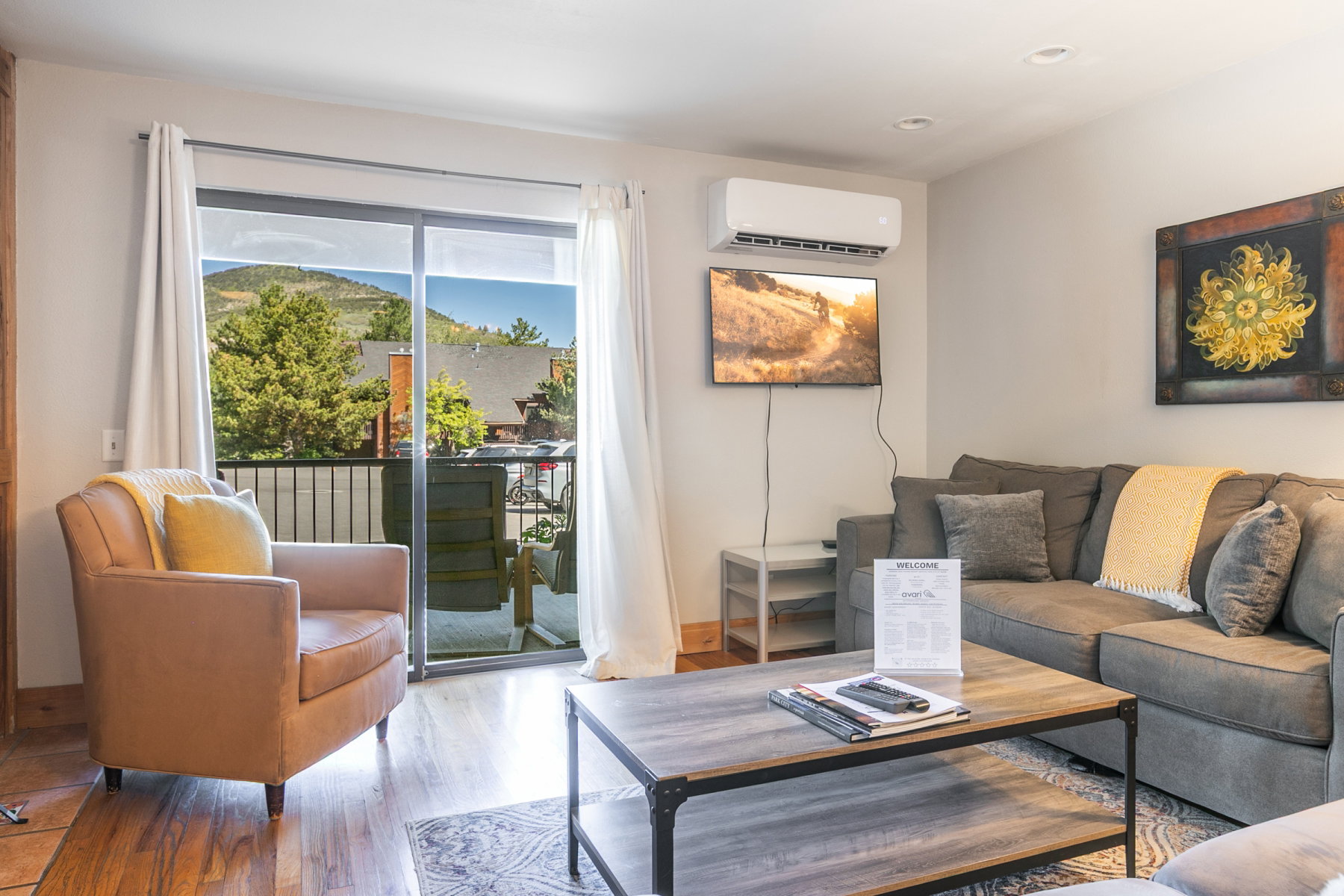 Living area featuring wood-finish flooring, a wall-mounted air conditioning unit, recessed lighting, and a sliding glass door opening to a private balcony with a black metal railing