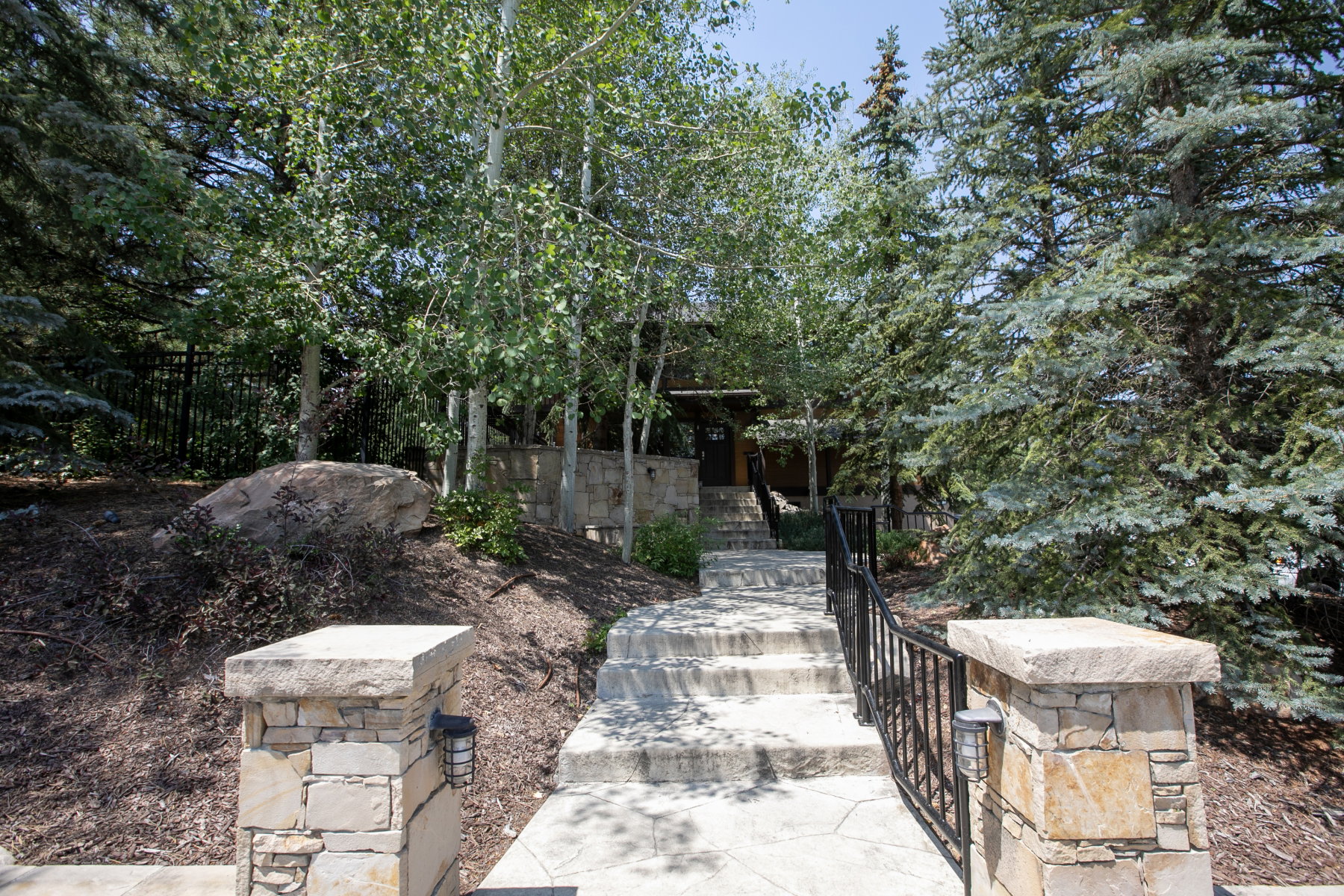 Stone entry pillars with integrated lighting and a black metal railing border a stone staircase leading to the property entrance