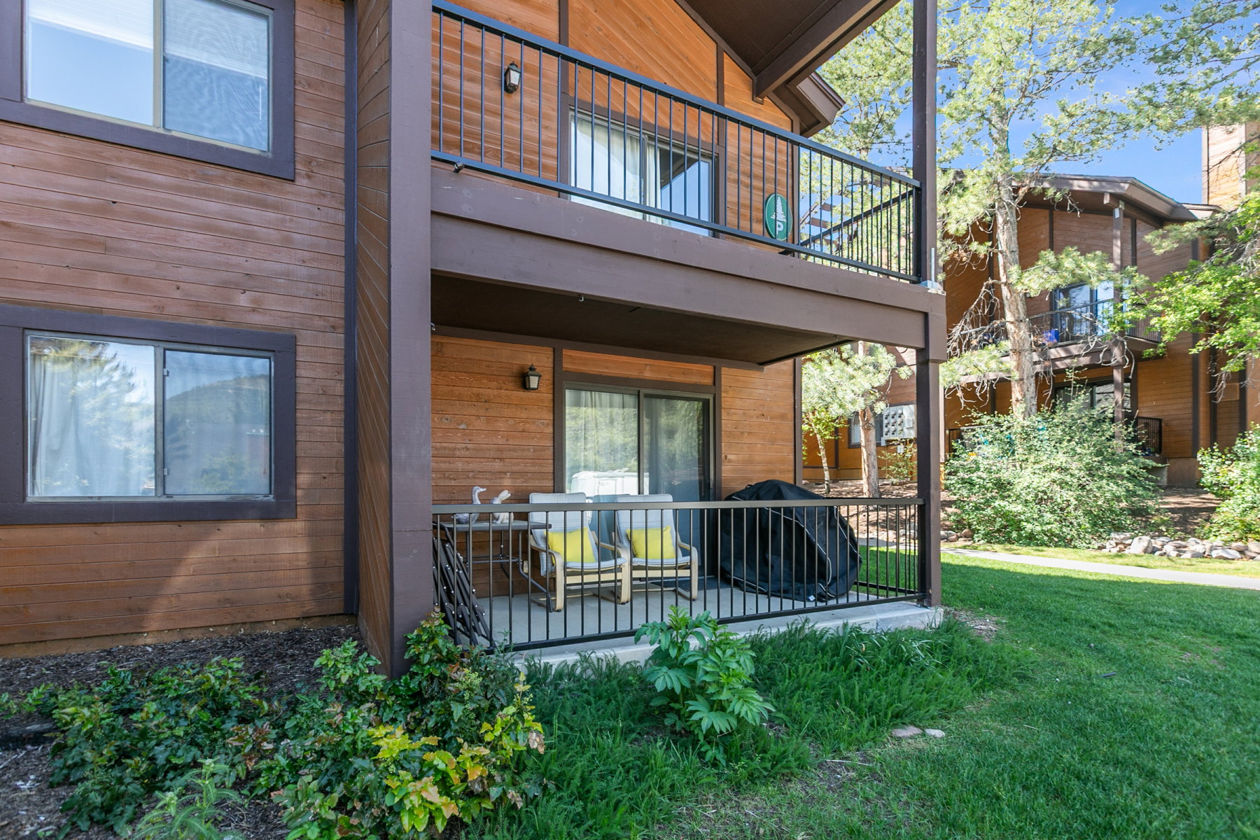 Wood-finish exterior featuring a ground-level patio and an upper-level balcony, both with dark metal railings