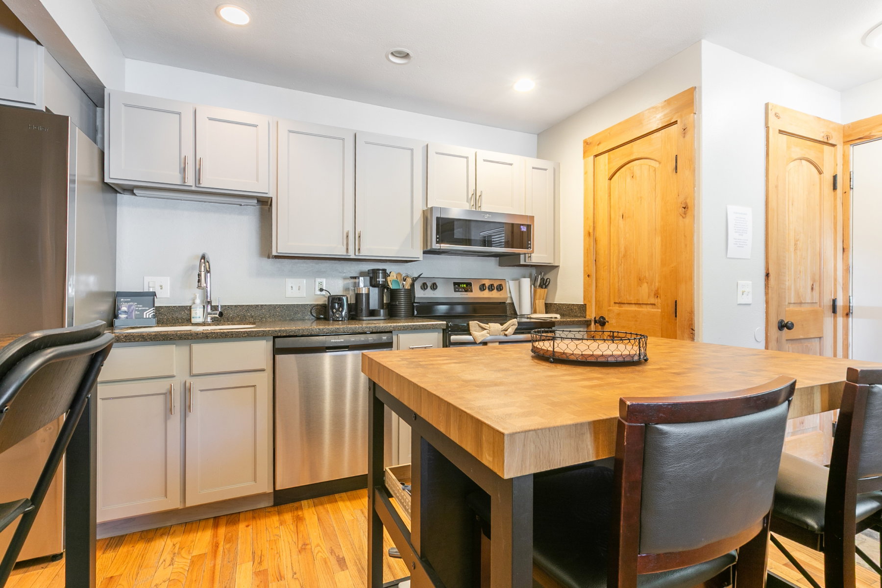 Kitchen featuring light gray cabinetry, stainless steel appliances, dark countertop, wood-finish flooring, and a butcher block island