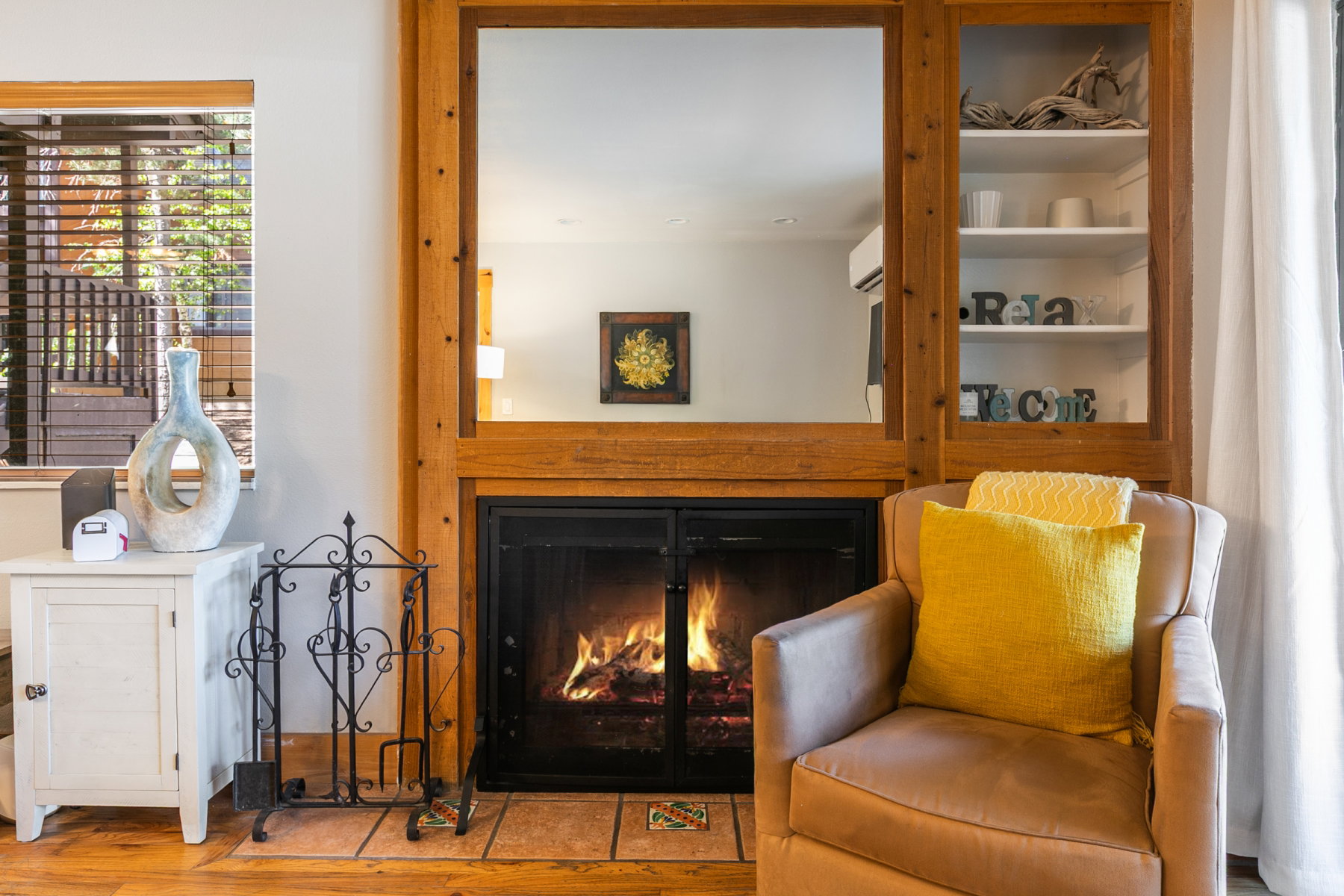 Wood-finish flooring anchors a living space featuring a fireplace with a black metal screen and a tiled hearth