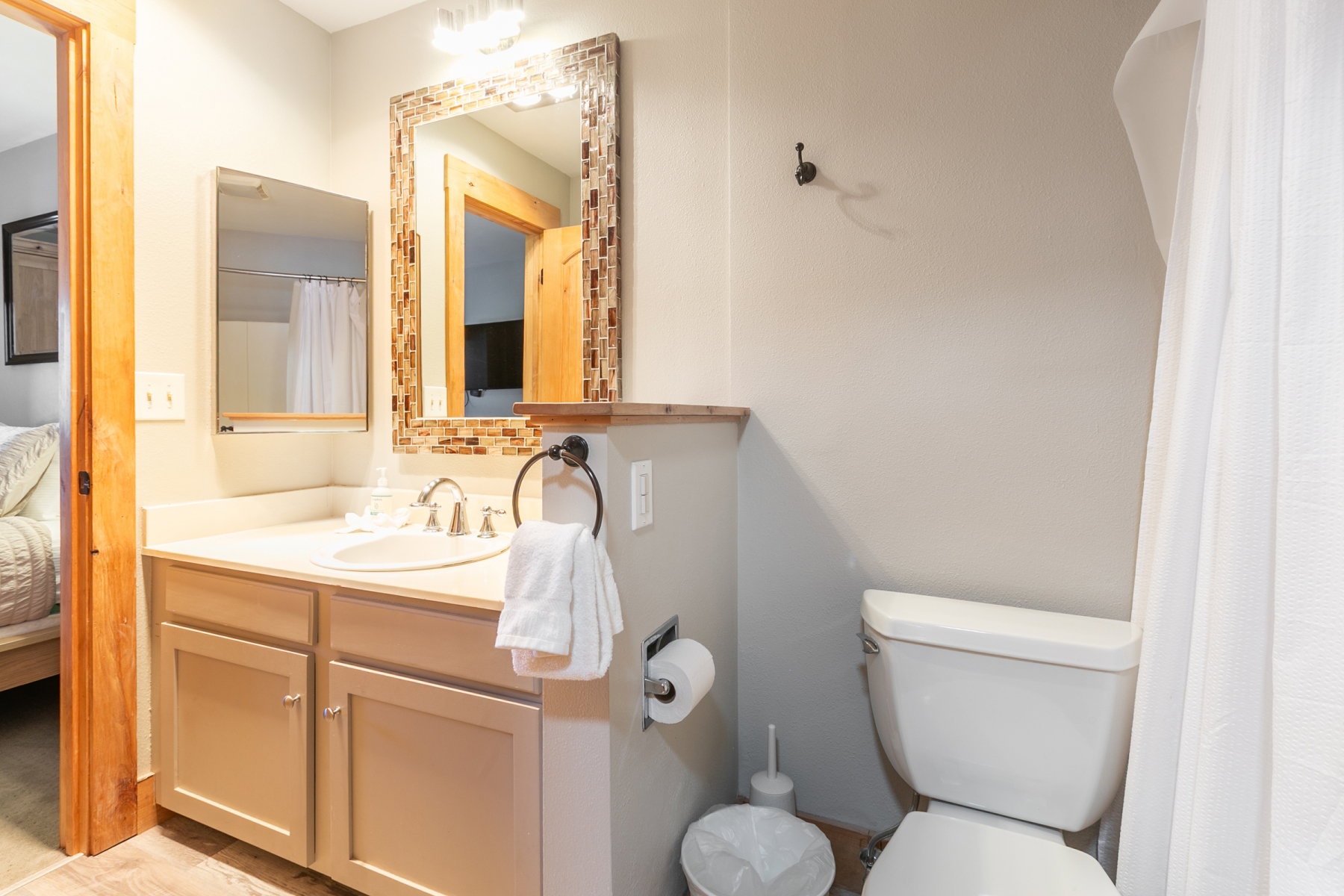 Bathroom featuring a light-toned vanity with an integrated sink, a mosaic-tiled framed mirror, a wall-mounted light fixture, and a toilet