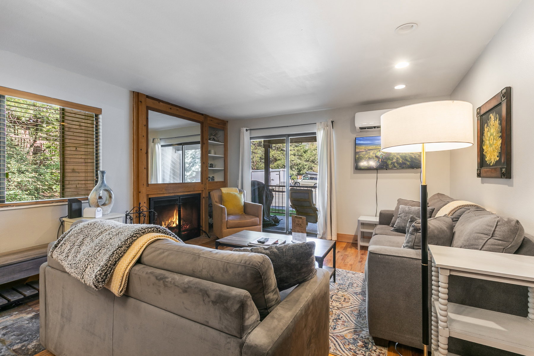 Living area featuring wood-finish flooring, a wood-framed fireplace with a mirror surround, built-in shelving, and recessed lighting