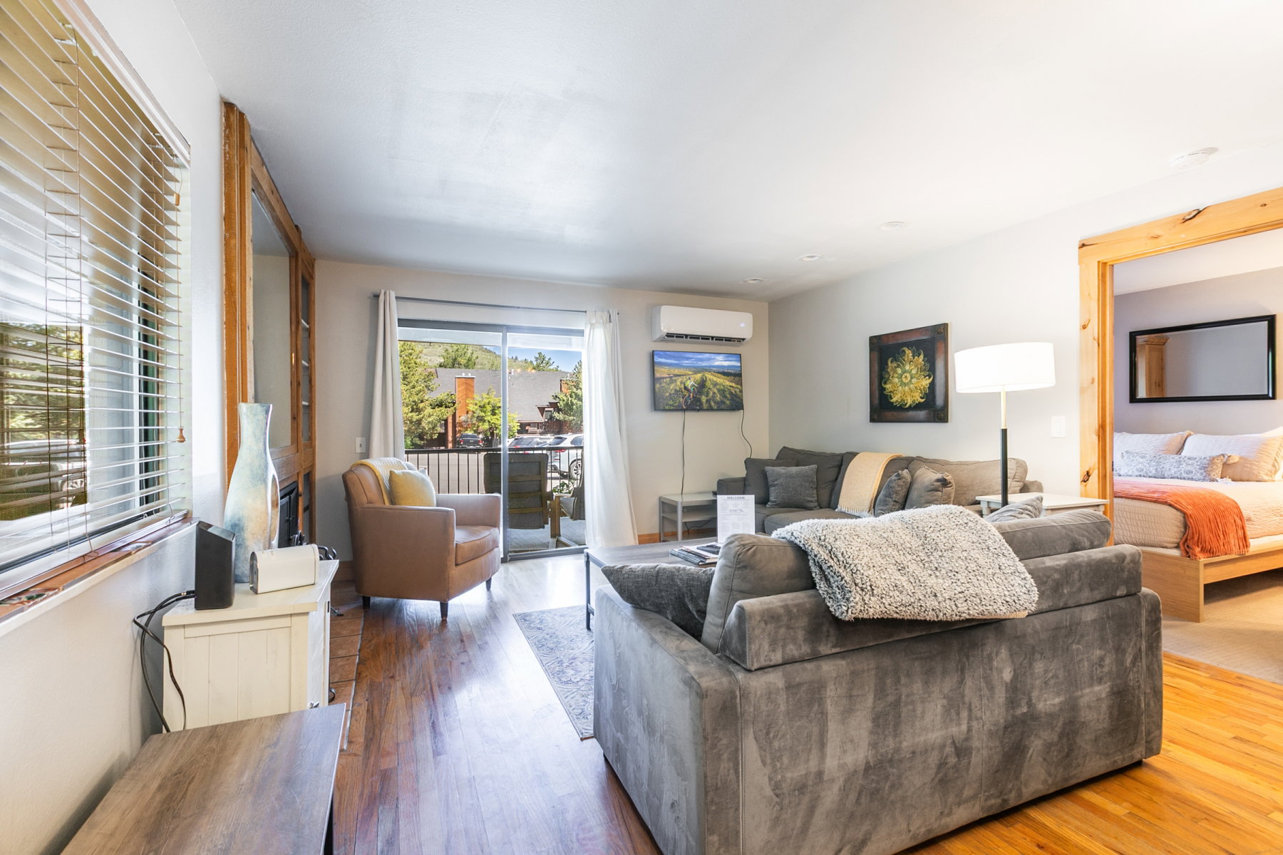 Living area featuring wood-finish flooring, a wall-mounted air conditioning unit, and a sliding glass door opening to an outdoor deck
