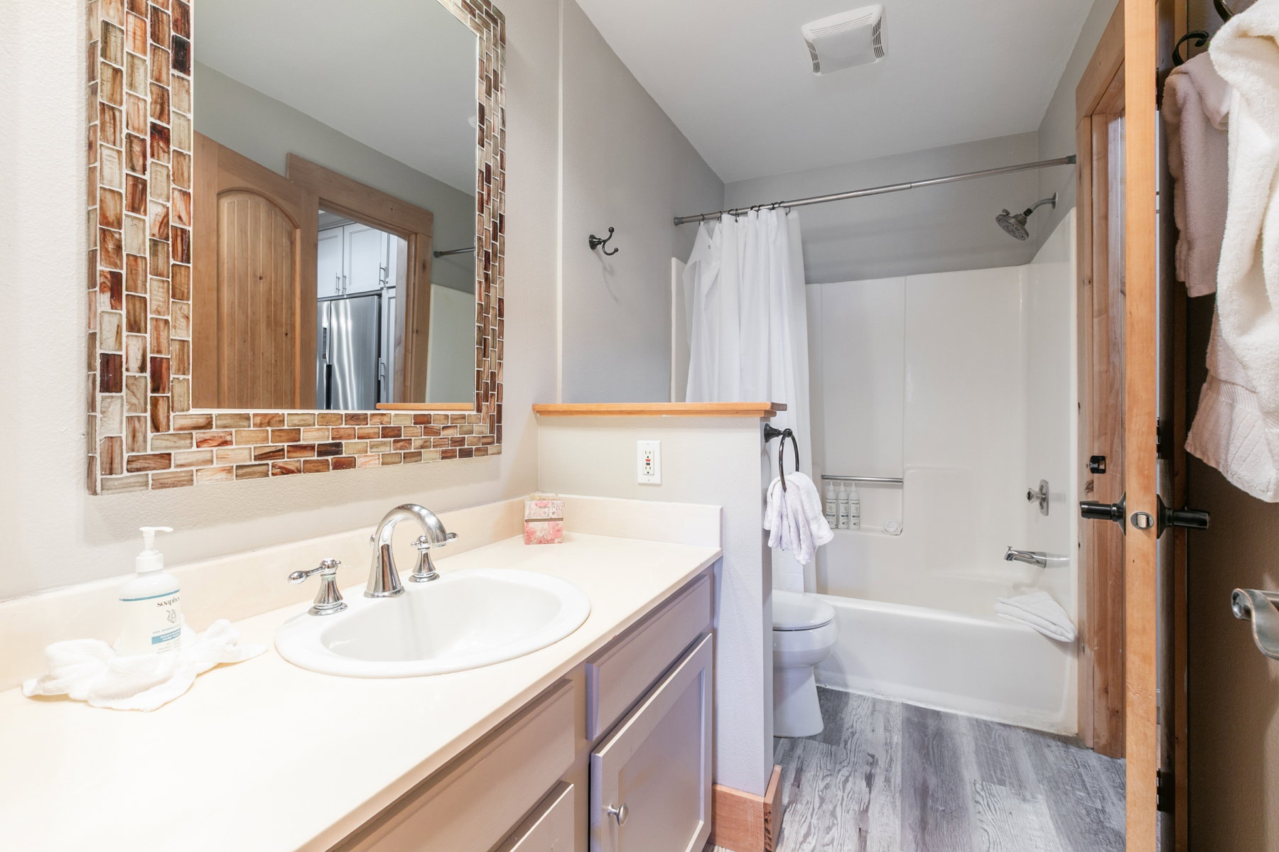 Bathroom featuring a vanity with a drop-in sink and a chrome faucet, a mosaic-tiled mirror, and wood-finish flooring