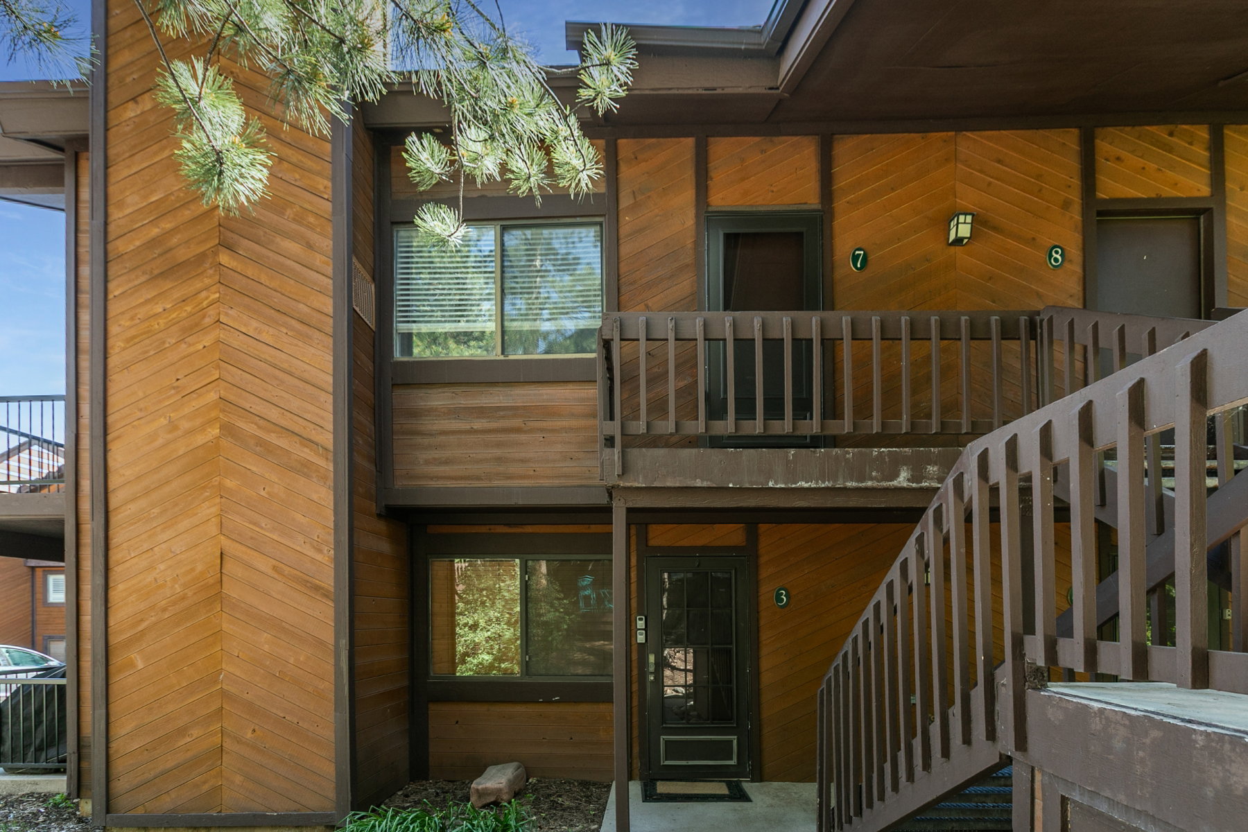 Wood-paneled exterior featuring a herringbone pattern, multiple windows with blinds, and an exterior staircase with matching railings