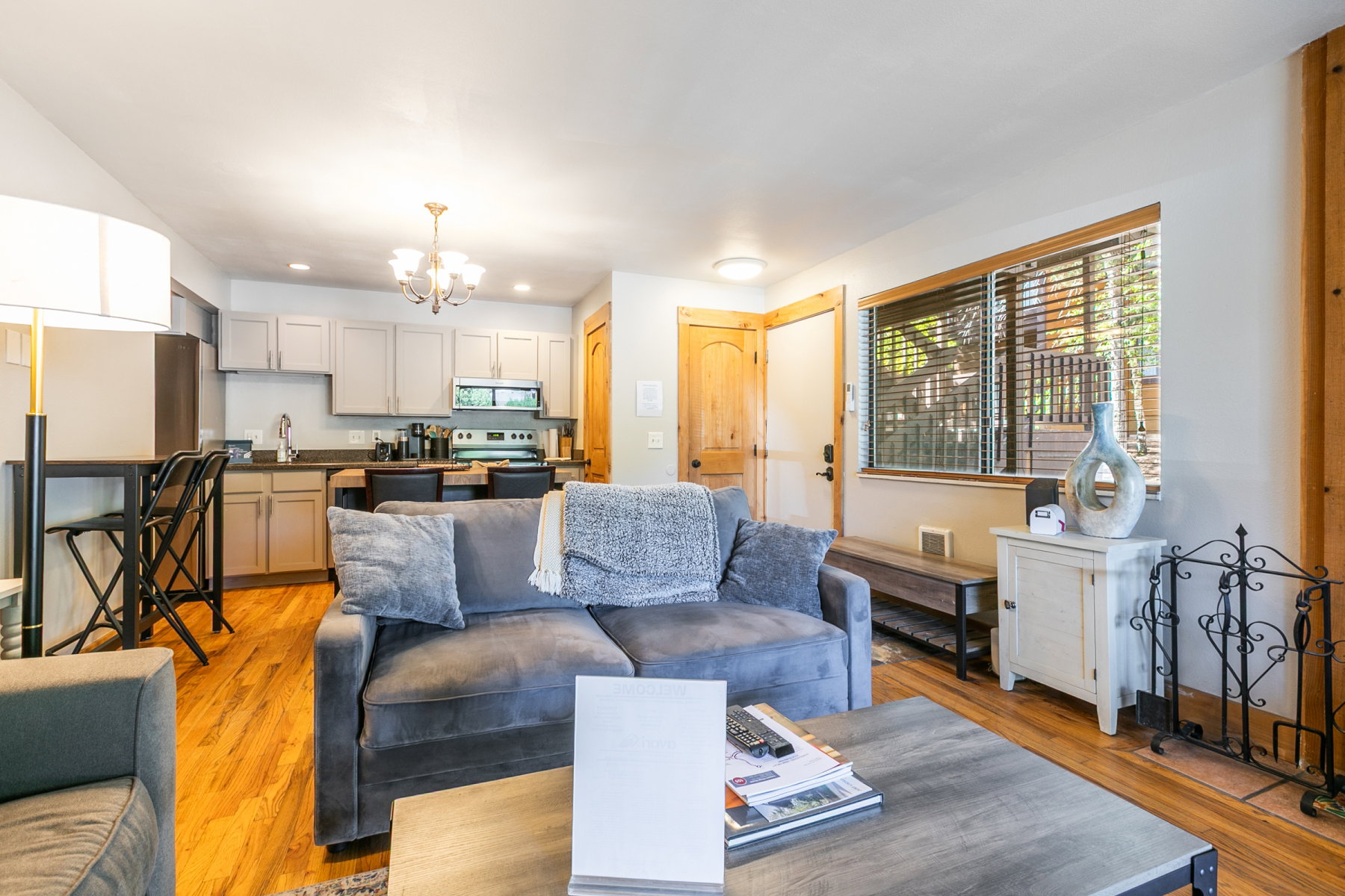 Open-concept living area featuring wood-finish flooring, a kitchen with light-colored cabinetry, a breakfast bar, and a window with horizontal blinds