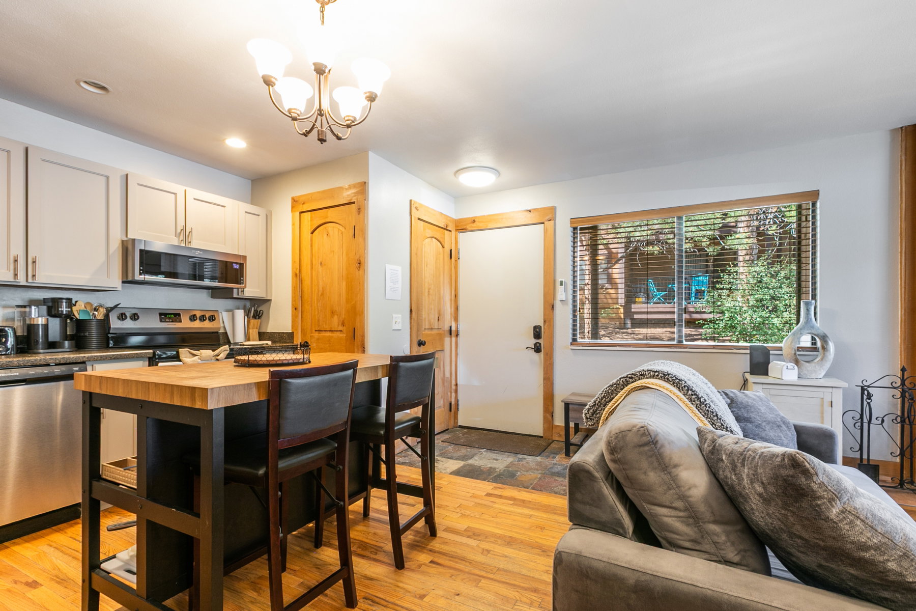Kitchen and living area featuring wood-finish flooring, stainless steel appliances, light-colored cabinetry, a butcher block island, and wood trim details