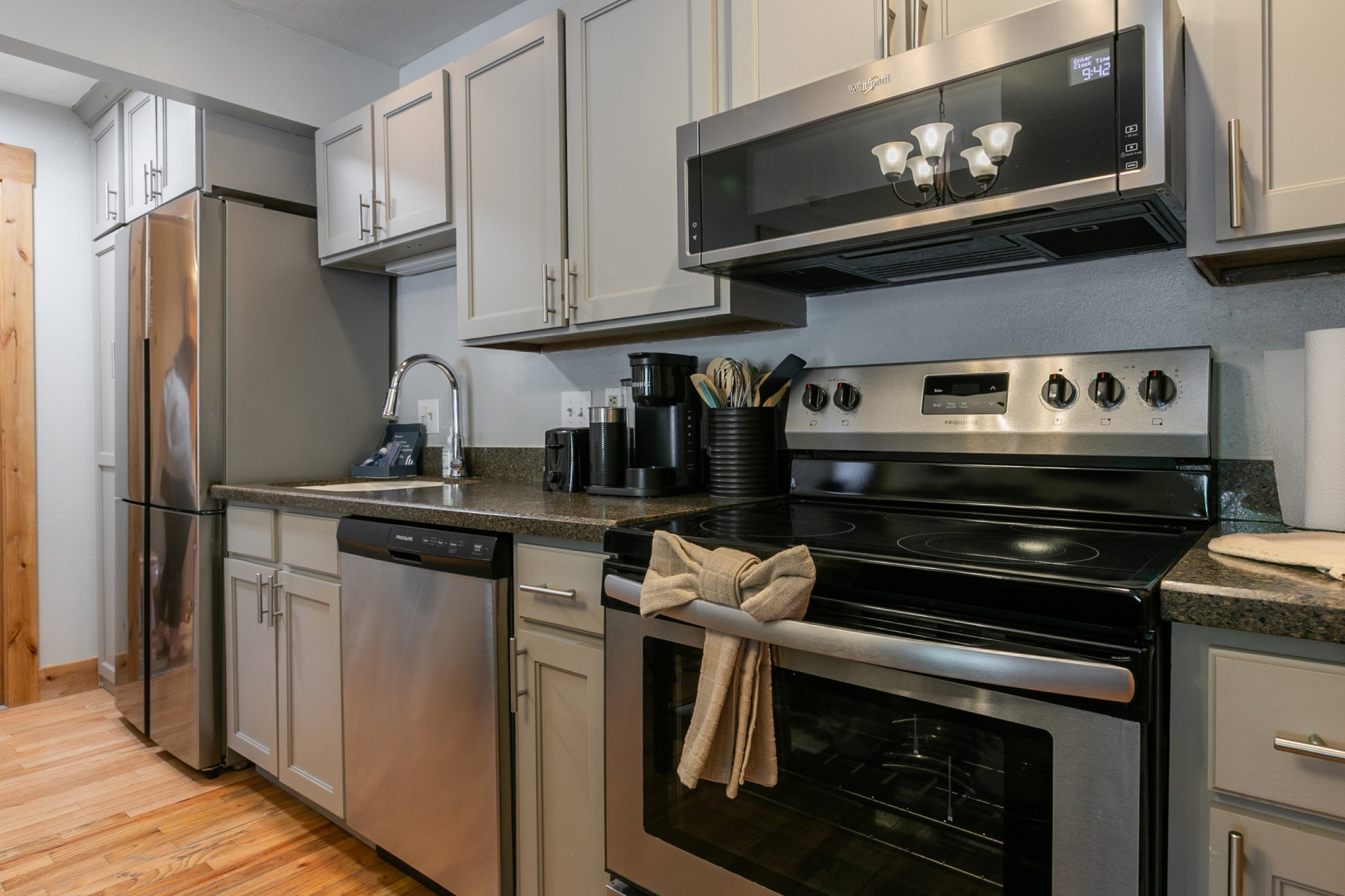 U-shaped kitchen featuring wood-finish flooring, stainless steel appliances, light gray cabinetry, dark speckled countertops, and a single basin sink with a gooseneck faucet