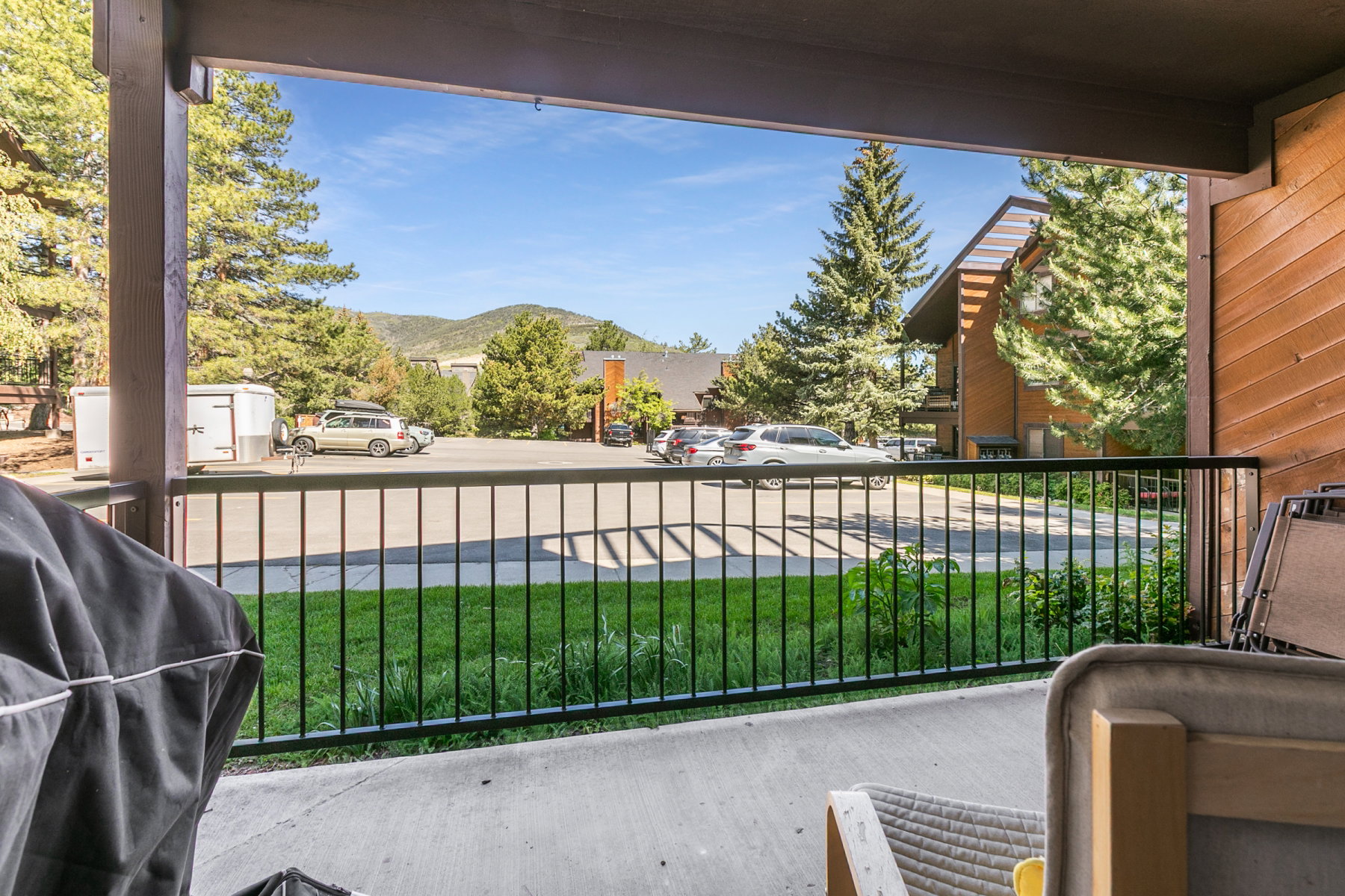 Spacious concrete patio with black metal railing, offering a backdrop of mature evergreen trees and distant mountain peaks