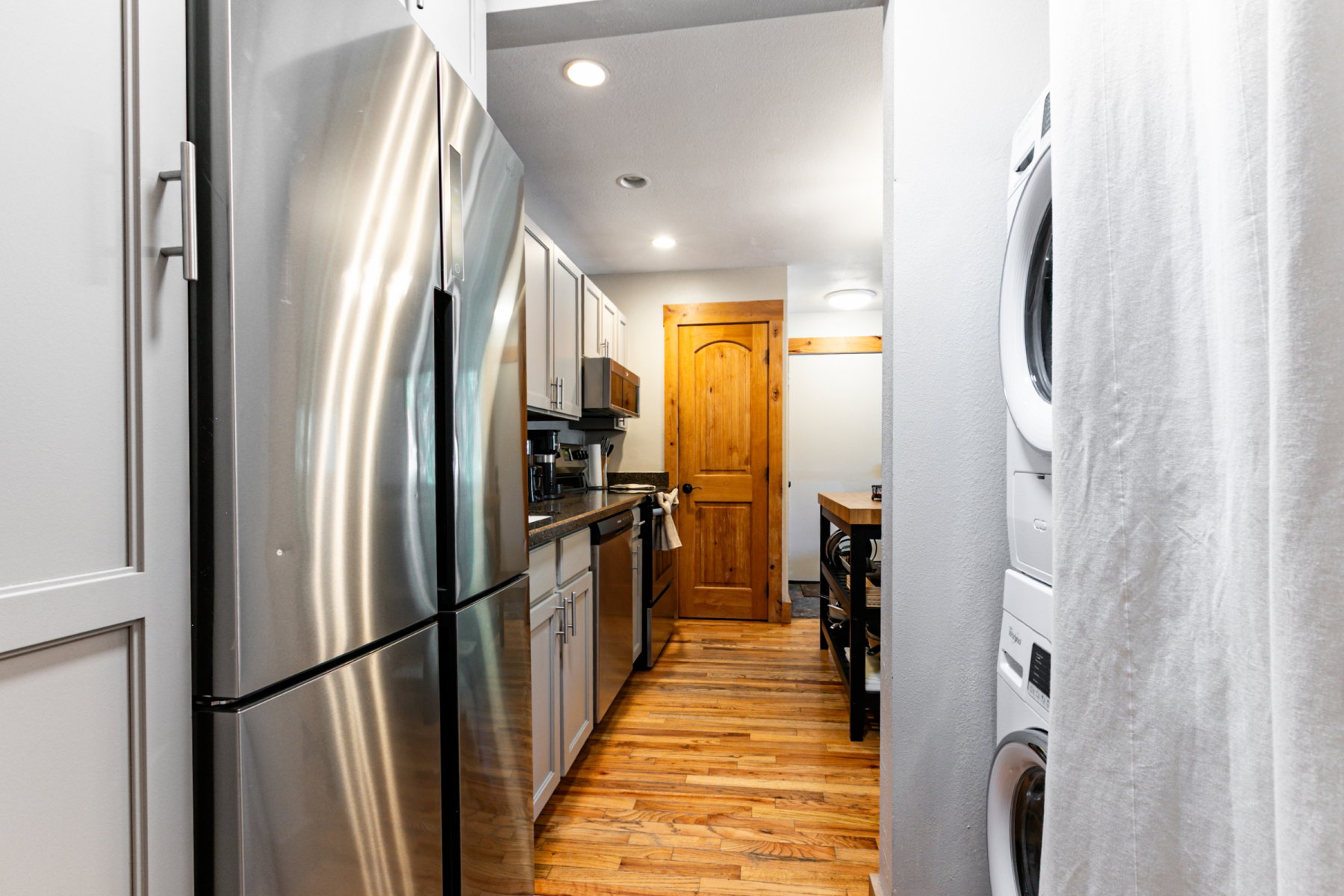 Kitchen featuring stainless steel appliances, light gray cabinetry, dark countertops, and wood-finish flooring