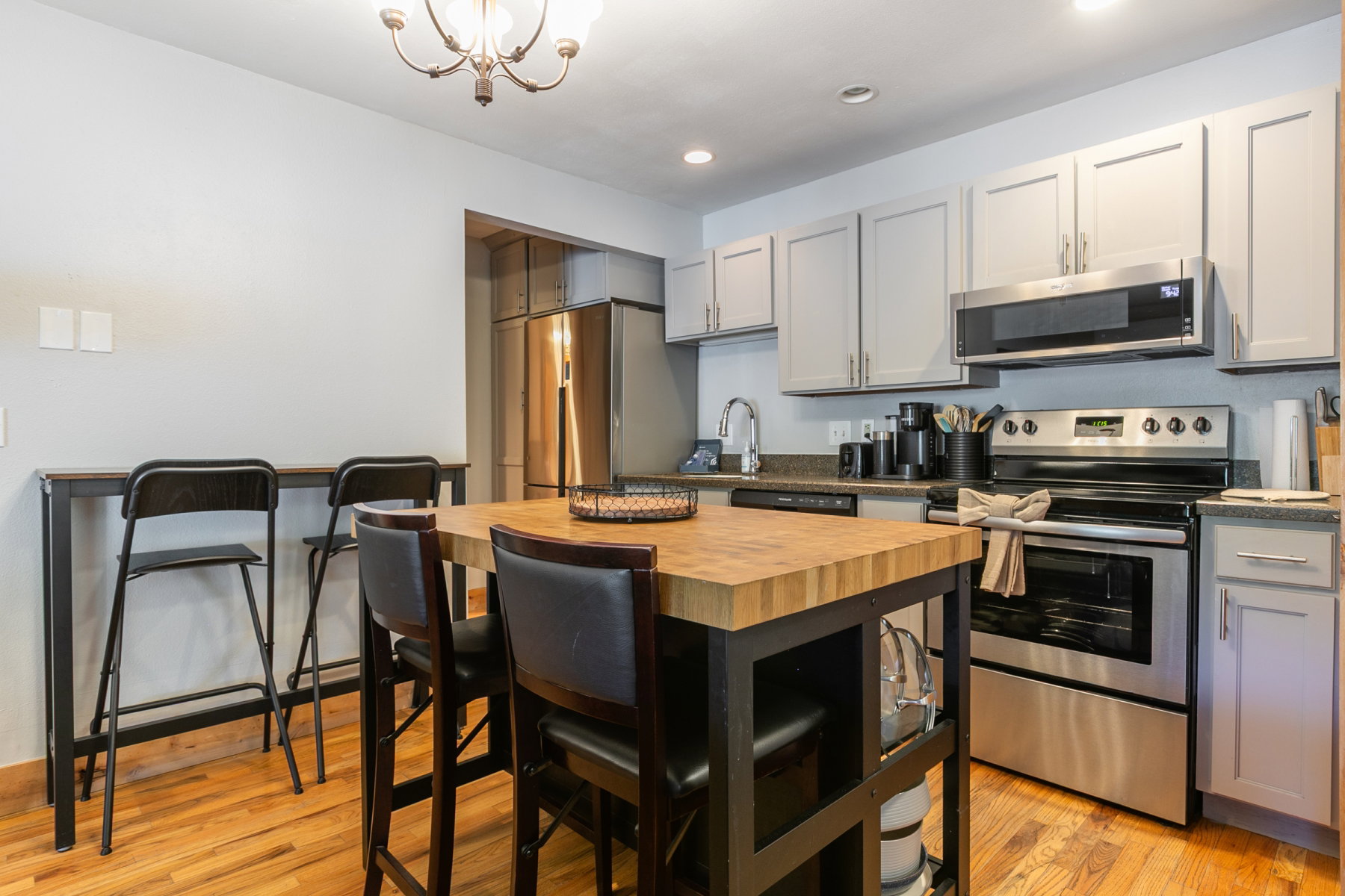 Kitchen featuring light gray cabinetry, stainless steel appliances, dark granite countertops, and wood-finish flooring