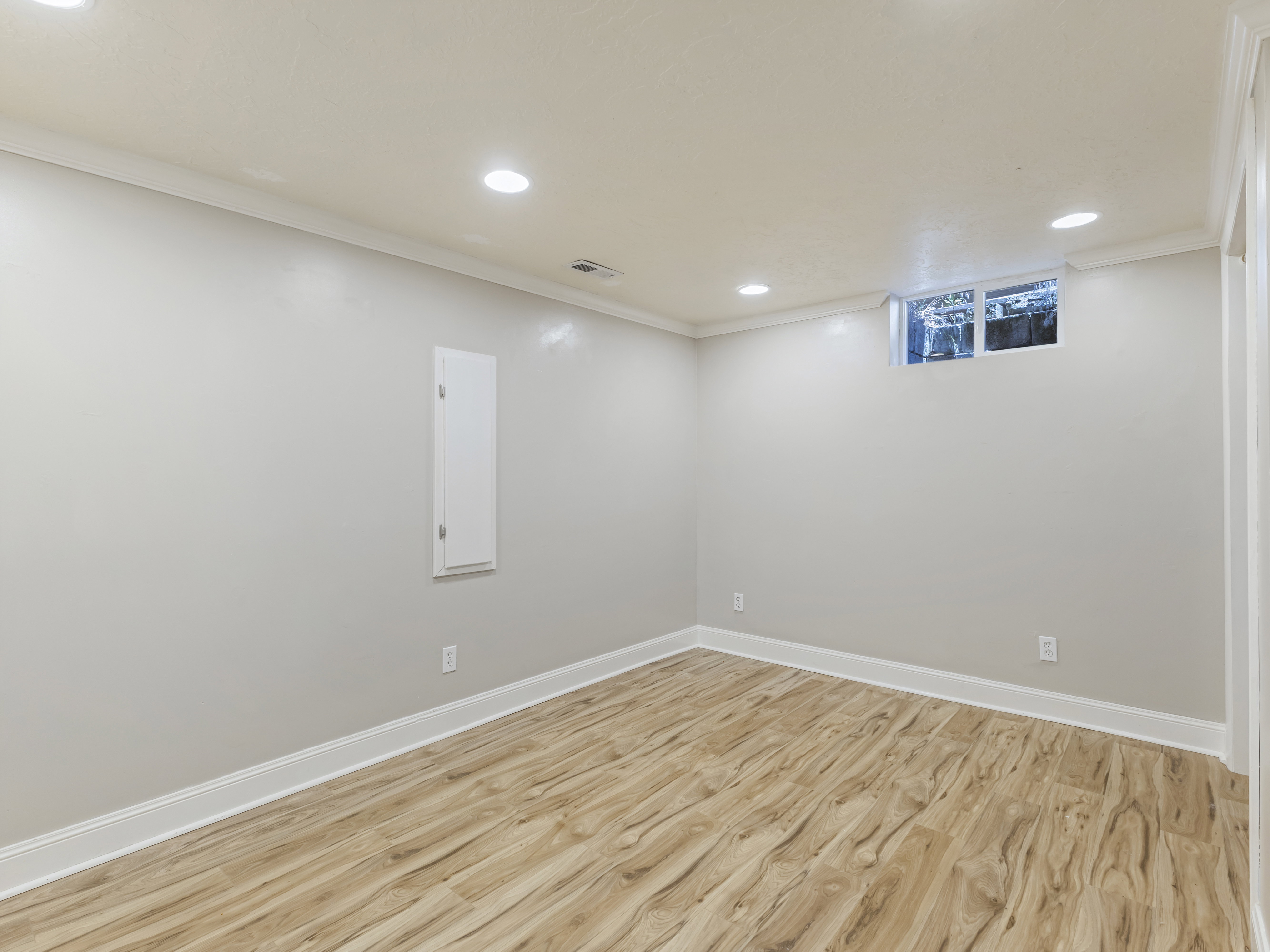 Spacious room featuring wood-finish flooring, recessed ceiling lighting, a single window, and crisp white baseboards and crown molding