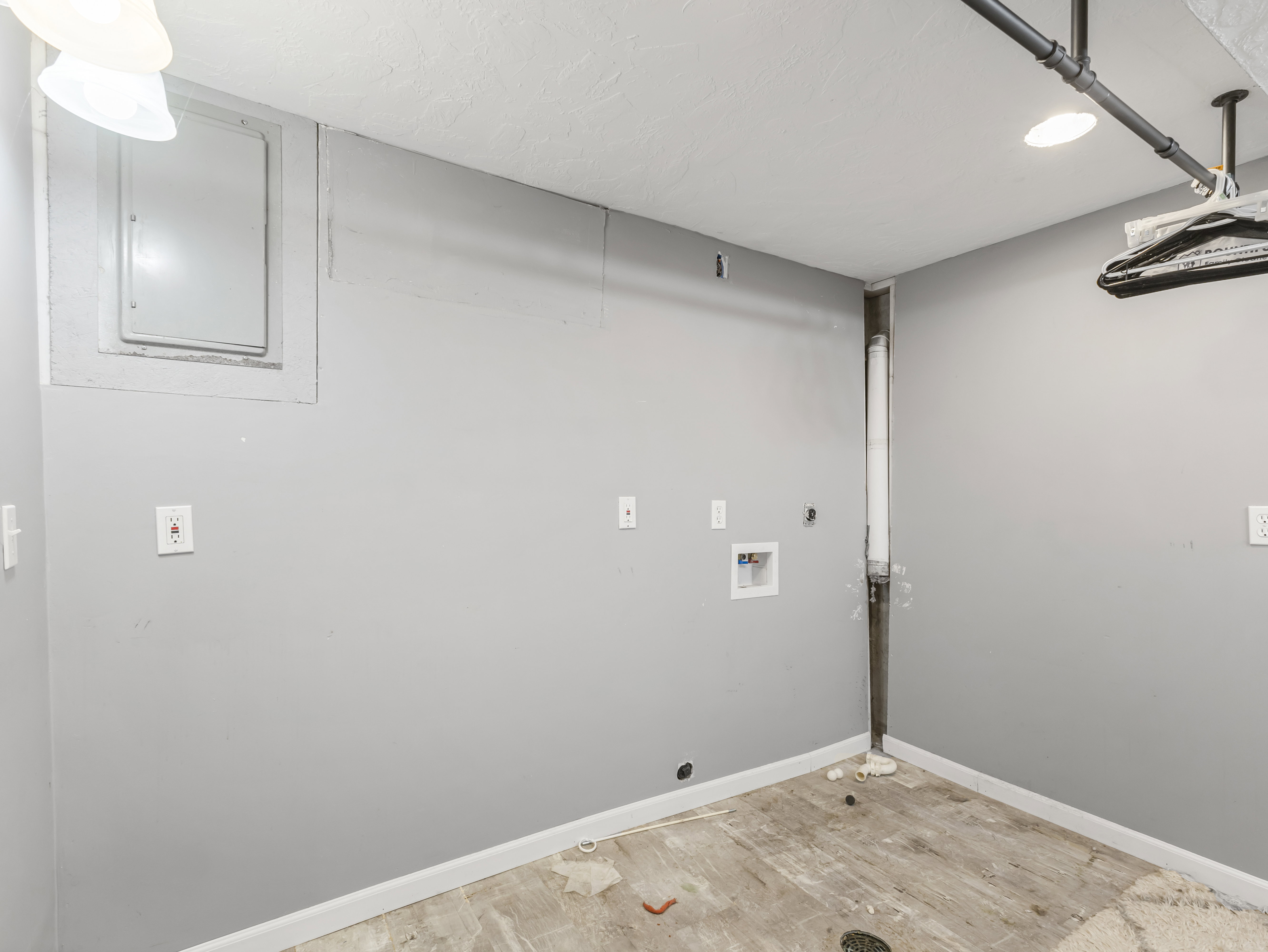 Laundry area with light gray walls, an exposed utility pipe, and a ceiling-mounted light fixture