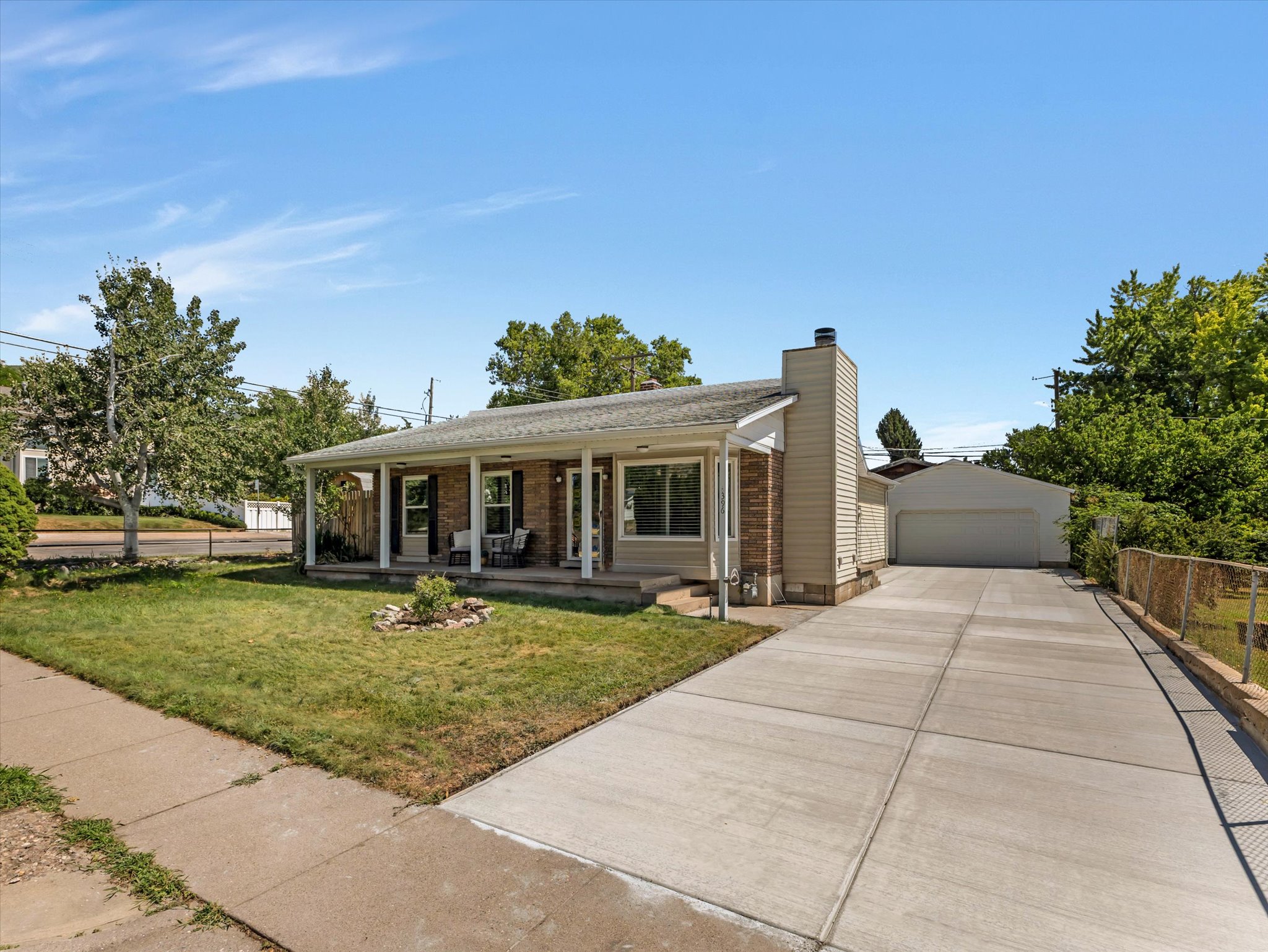 Brick facade home featuring a covered front porch, an extended concrete driveway, and a detached garage