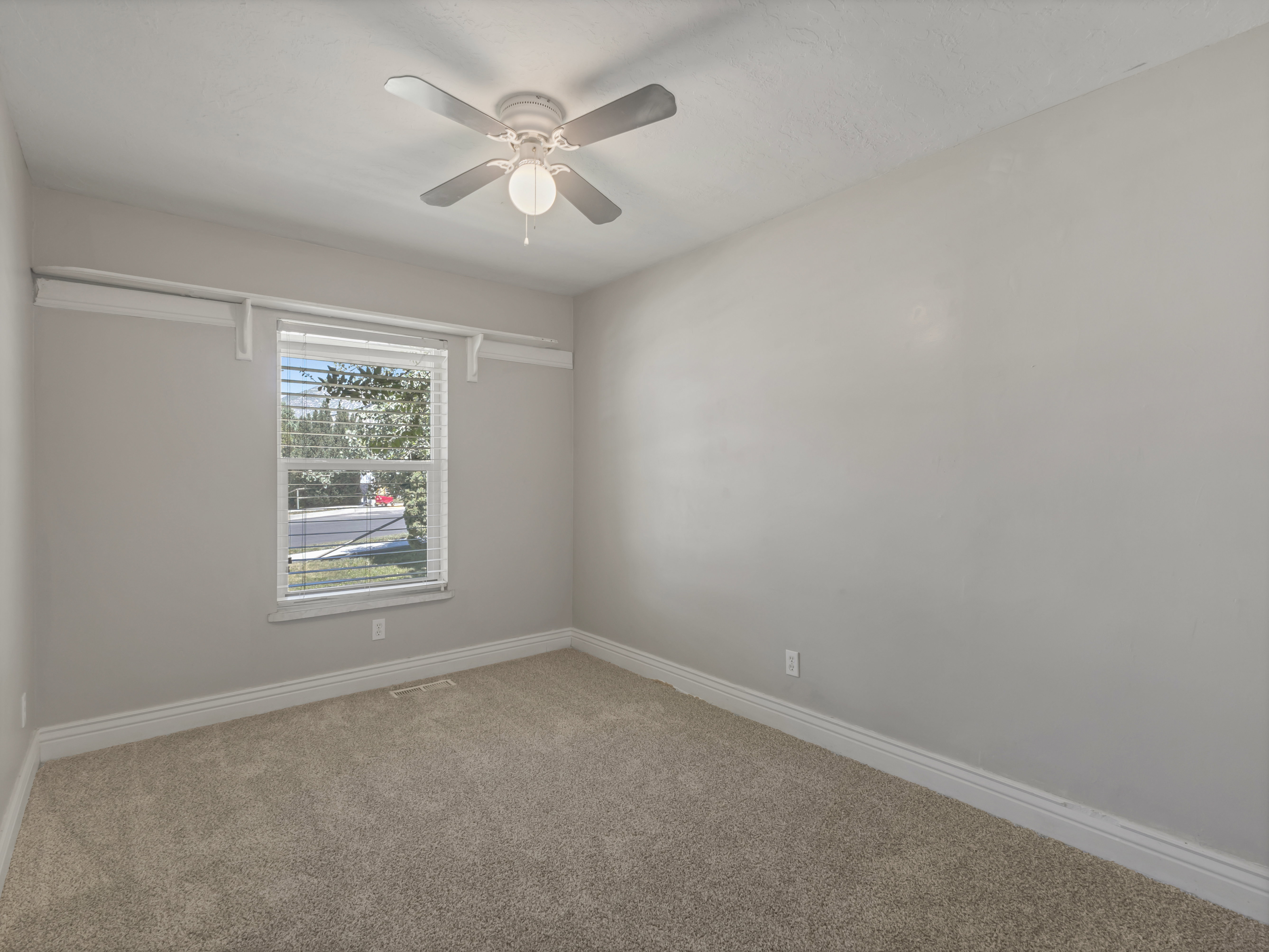 Neutral-toned wall paint and carpeting, window with horizontal blinds, built-in shelf with hanging rod, and ceiling fan with integrated lighting
