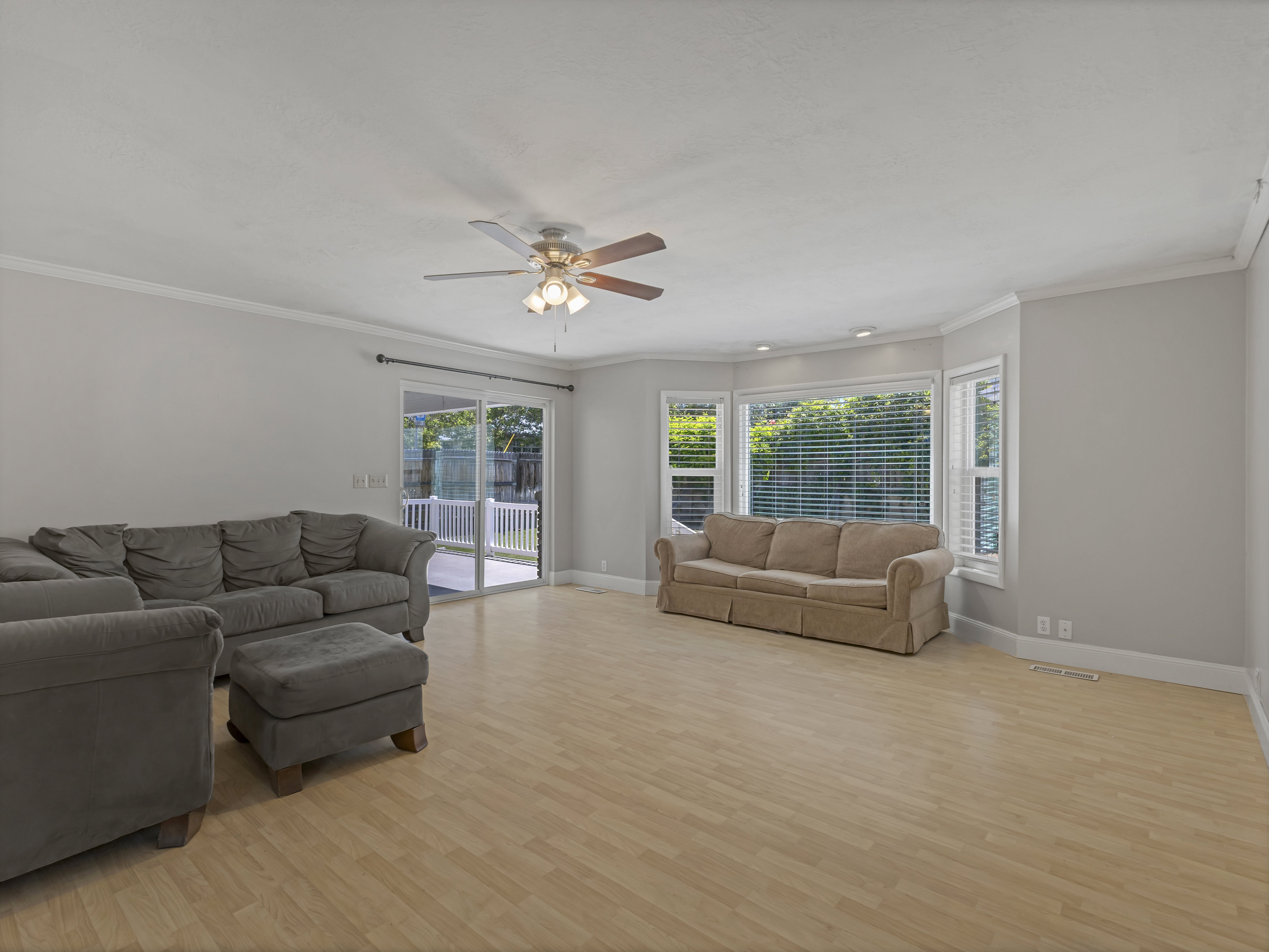 Spacious living area featuring light wood-finish flooring, a contemporary ceiling fan, and crown molding