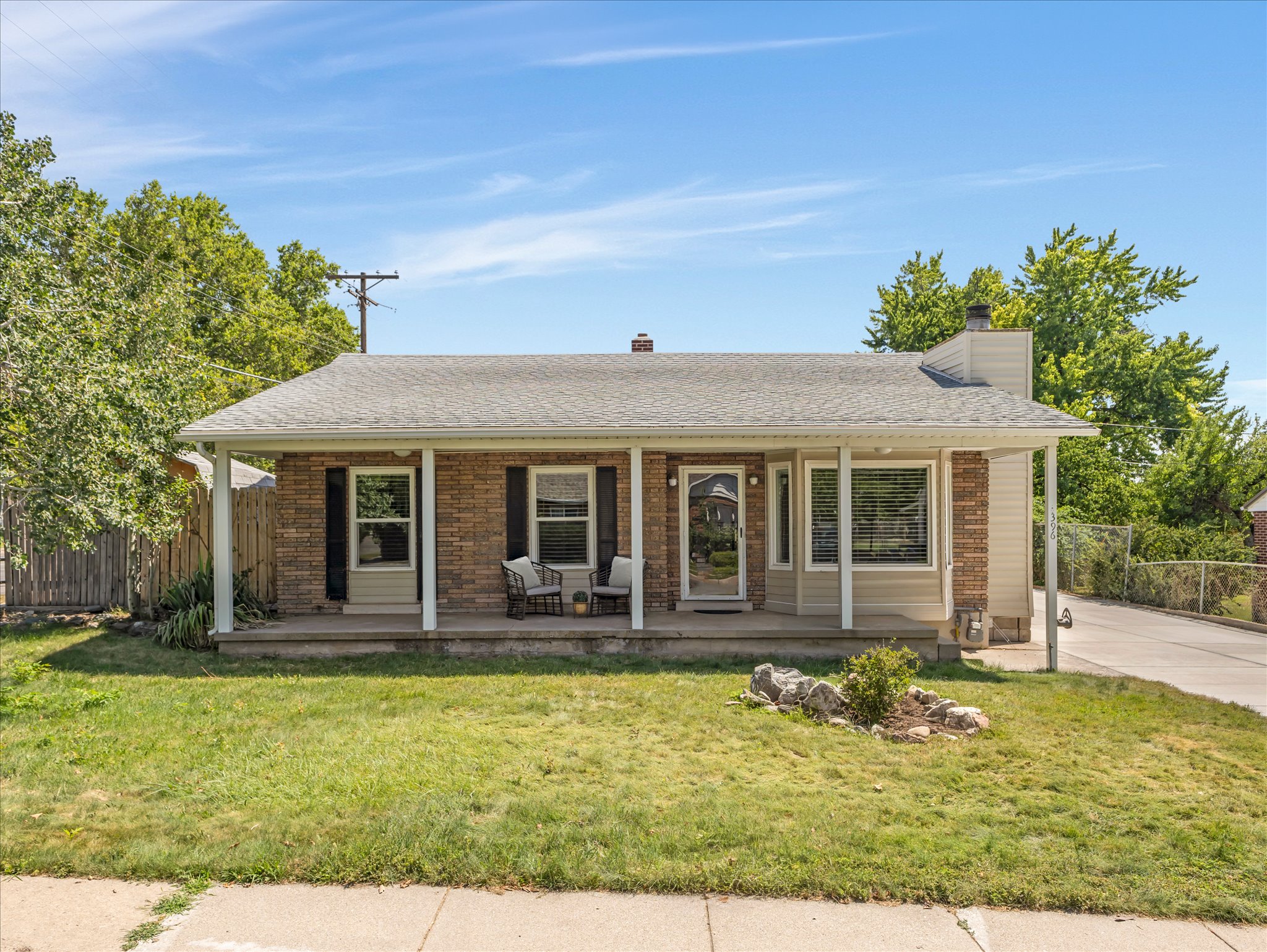 Brick and siding exterior featuring a covered front porch with white columns, a concrete driveway, and a fenced perimeter