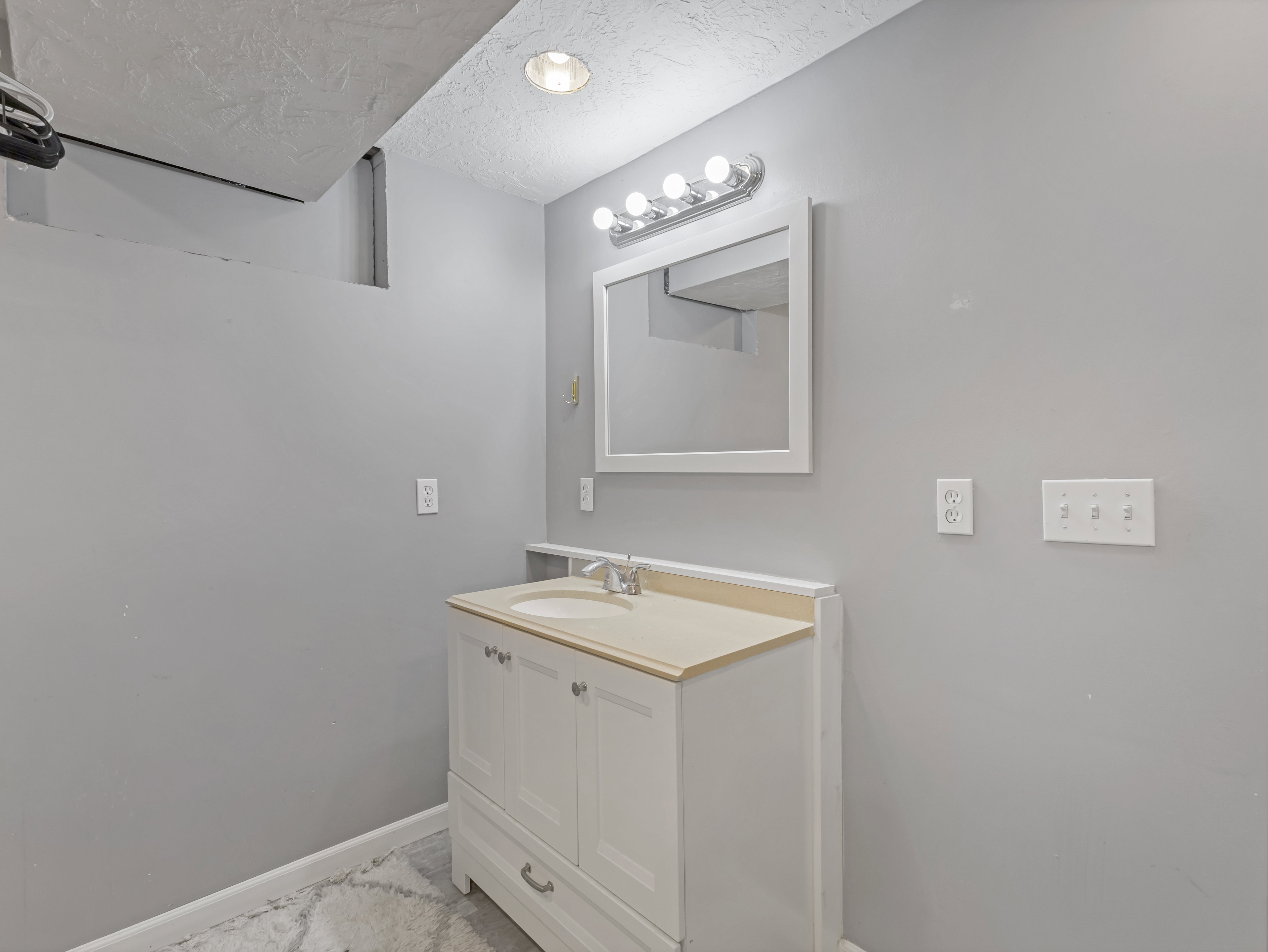 White vanity cabinet with integrated sink, framed mirror, and chrome vanity light fixture