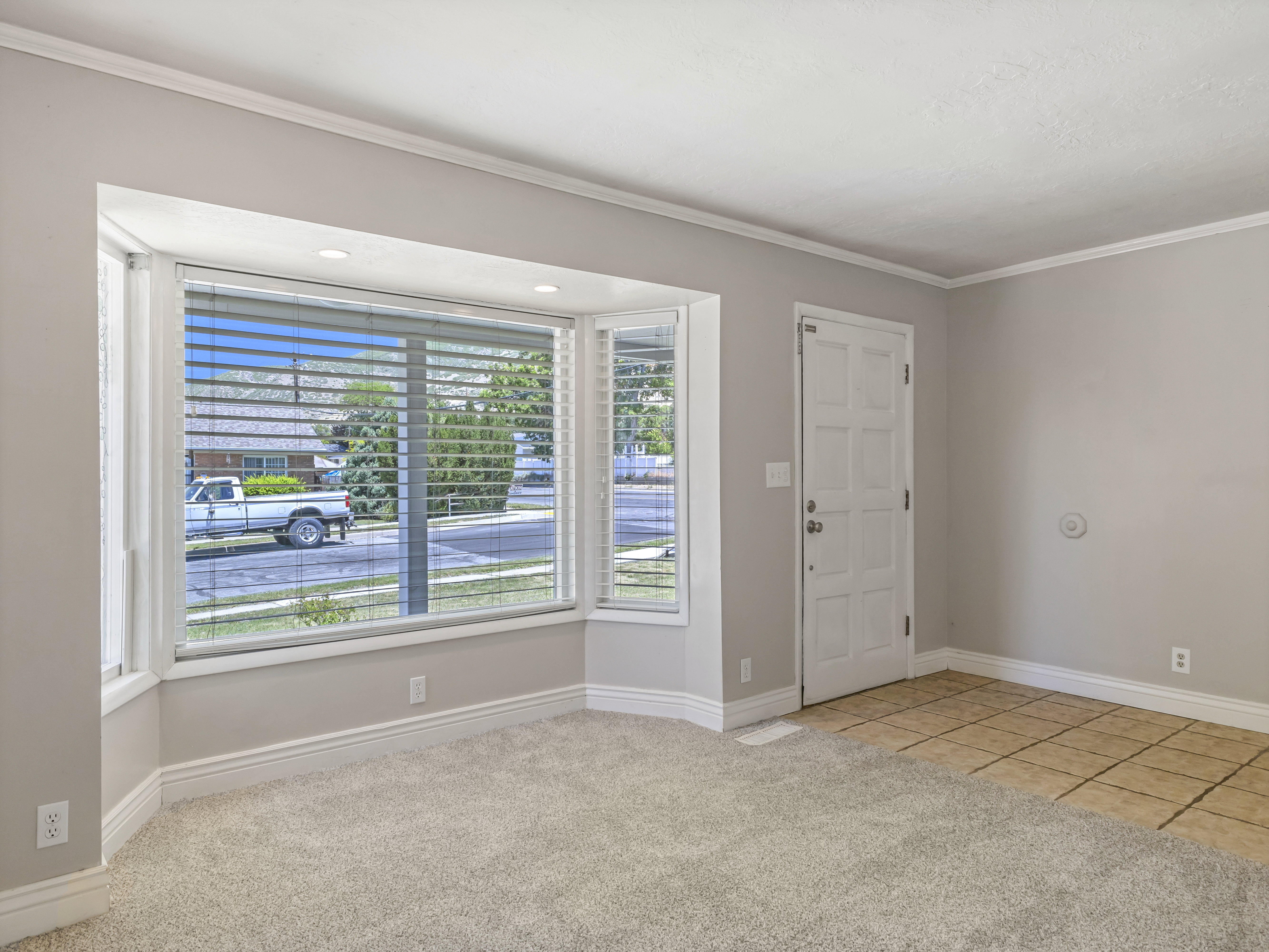 Bay window with integrated recessed lighting, light-colored carpeting, white baseboards, and a paneled entry door