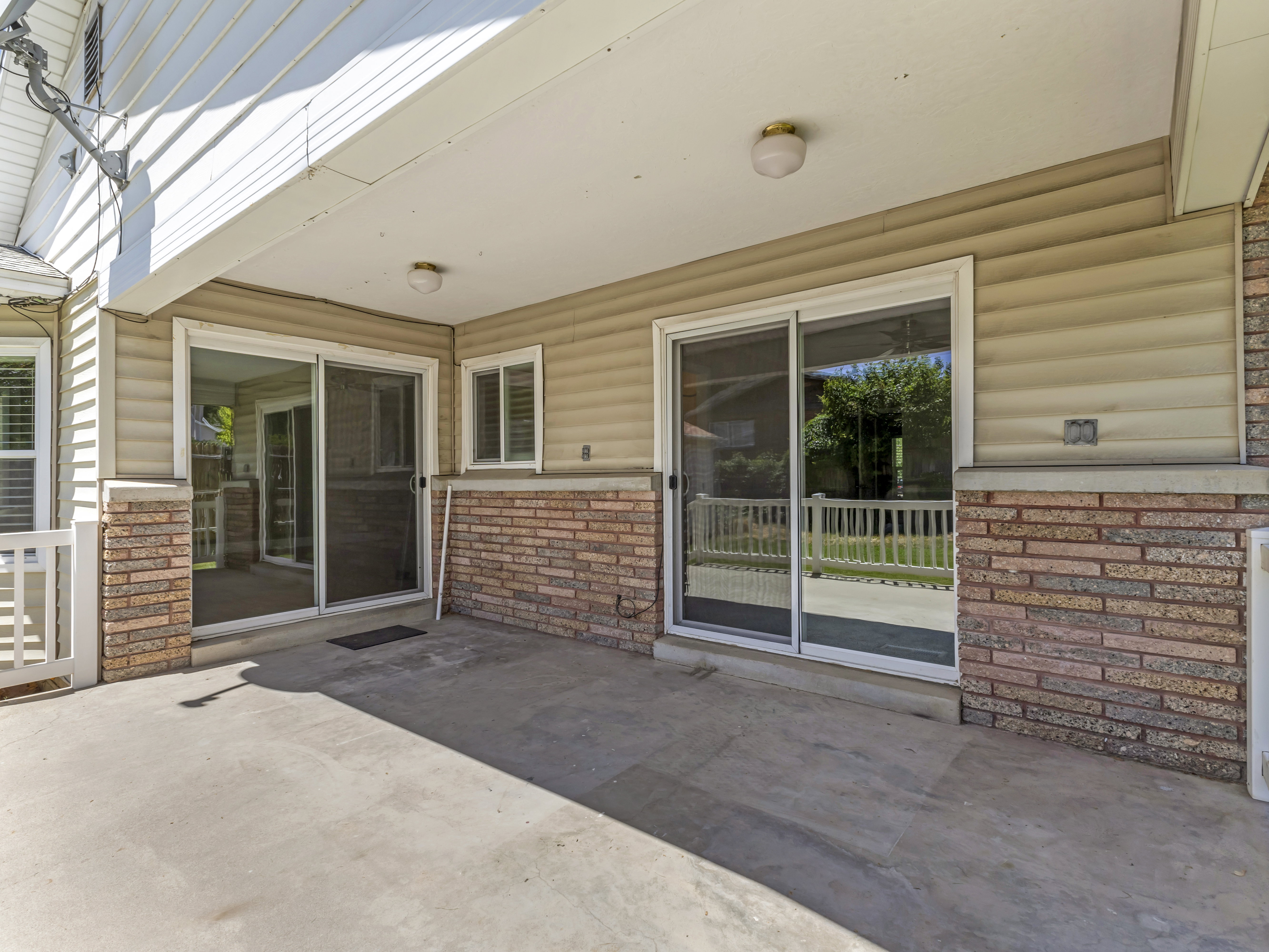 Covered concrete patio featuring two sets of sliding glass doors, horizontal siding, and brick veneer accents