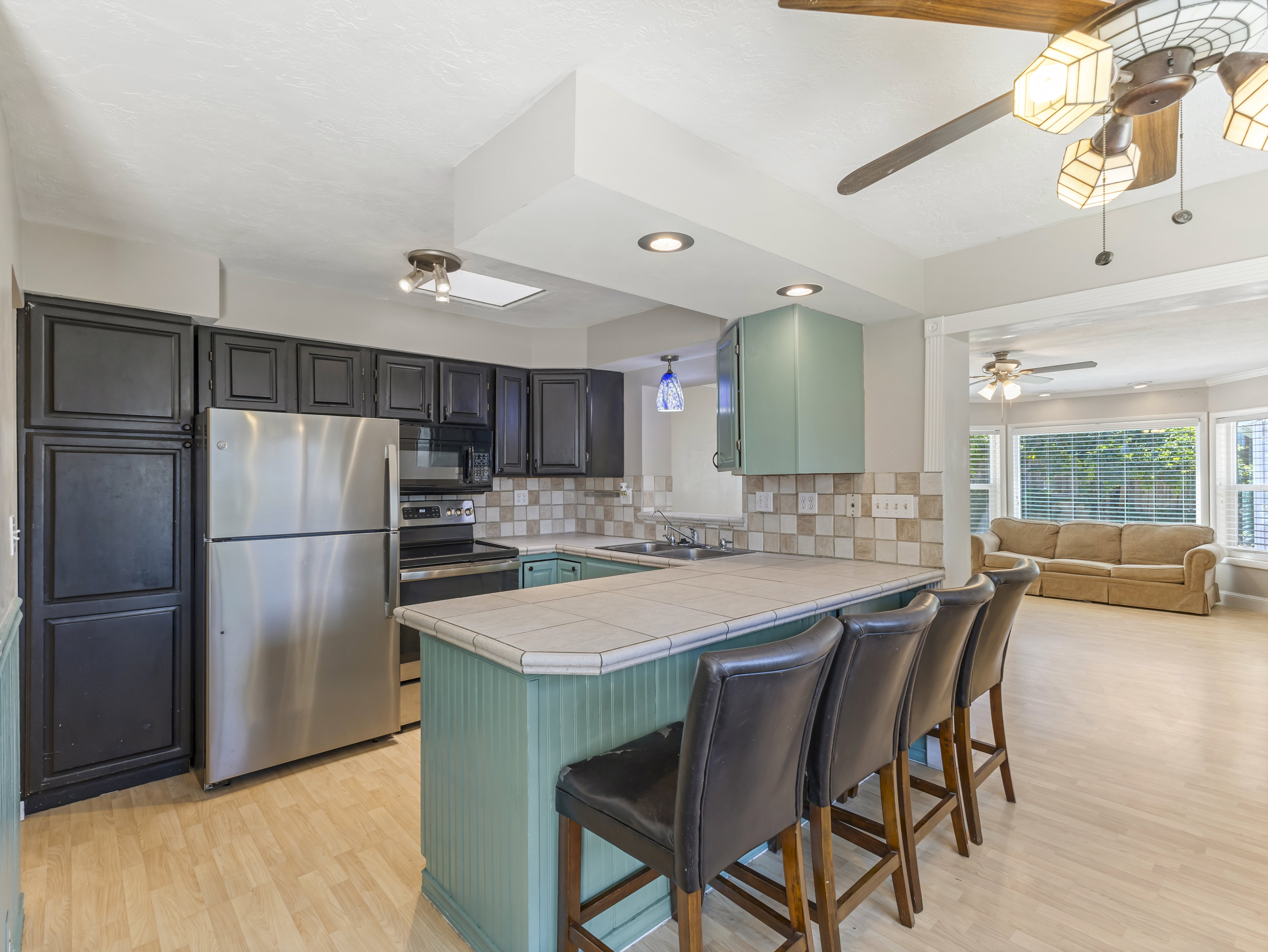 Kitchen featuring black paneled cabinetry, stainless steel appliances, a light-colored tile backsplash, and a breakfast bar with beadboard paneling
