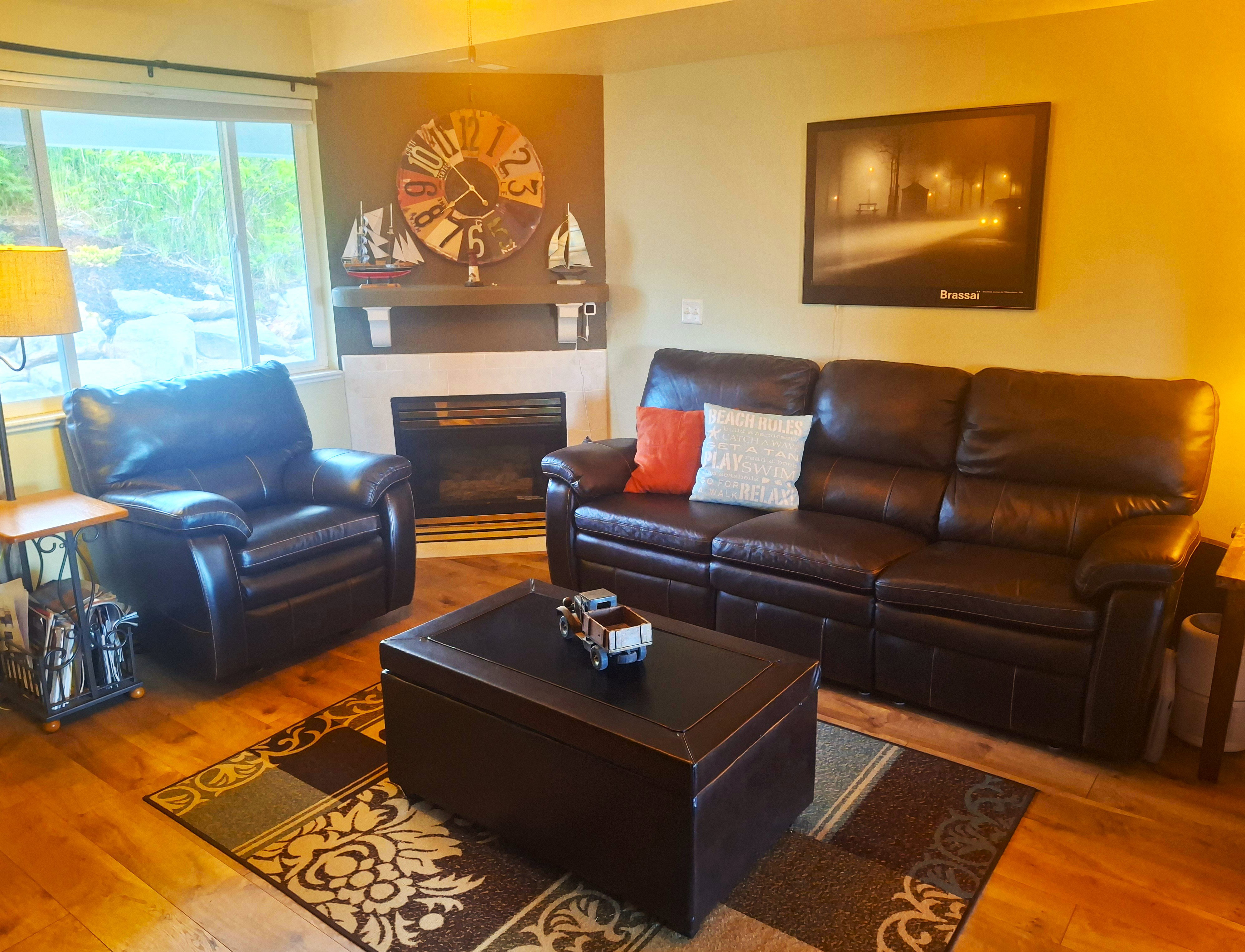 Living area featuring wood-finish flooring, a corner fireplace with a mantel, and a large window