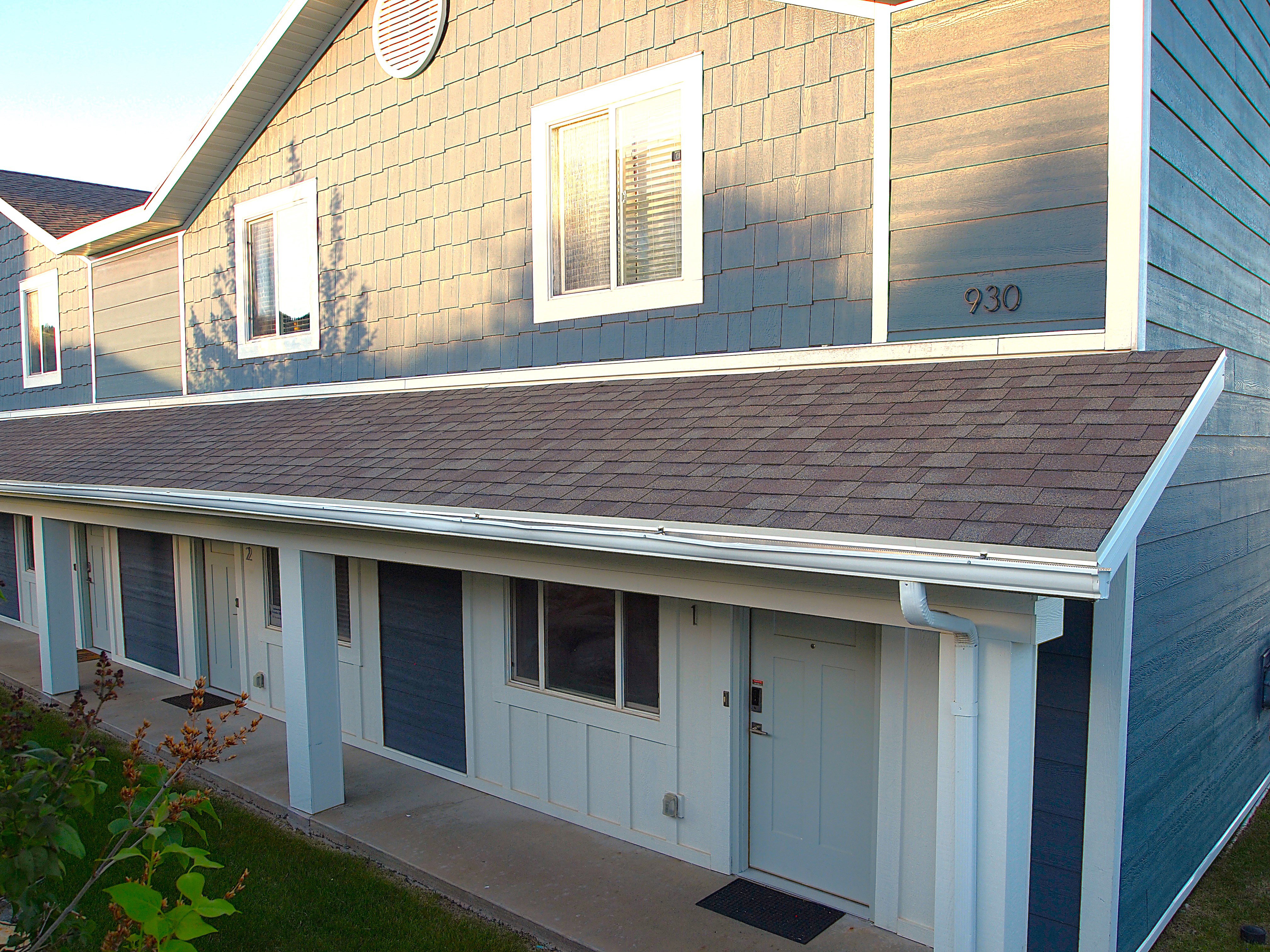 Multi-unit exterior with a covered entry, featuring asphalt shingle roofing, white gutters, and light blue siding