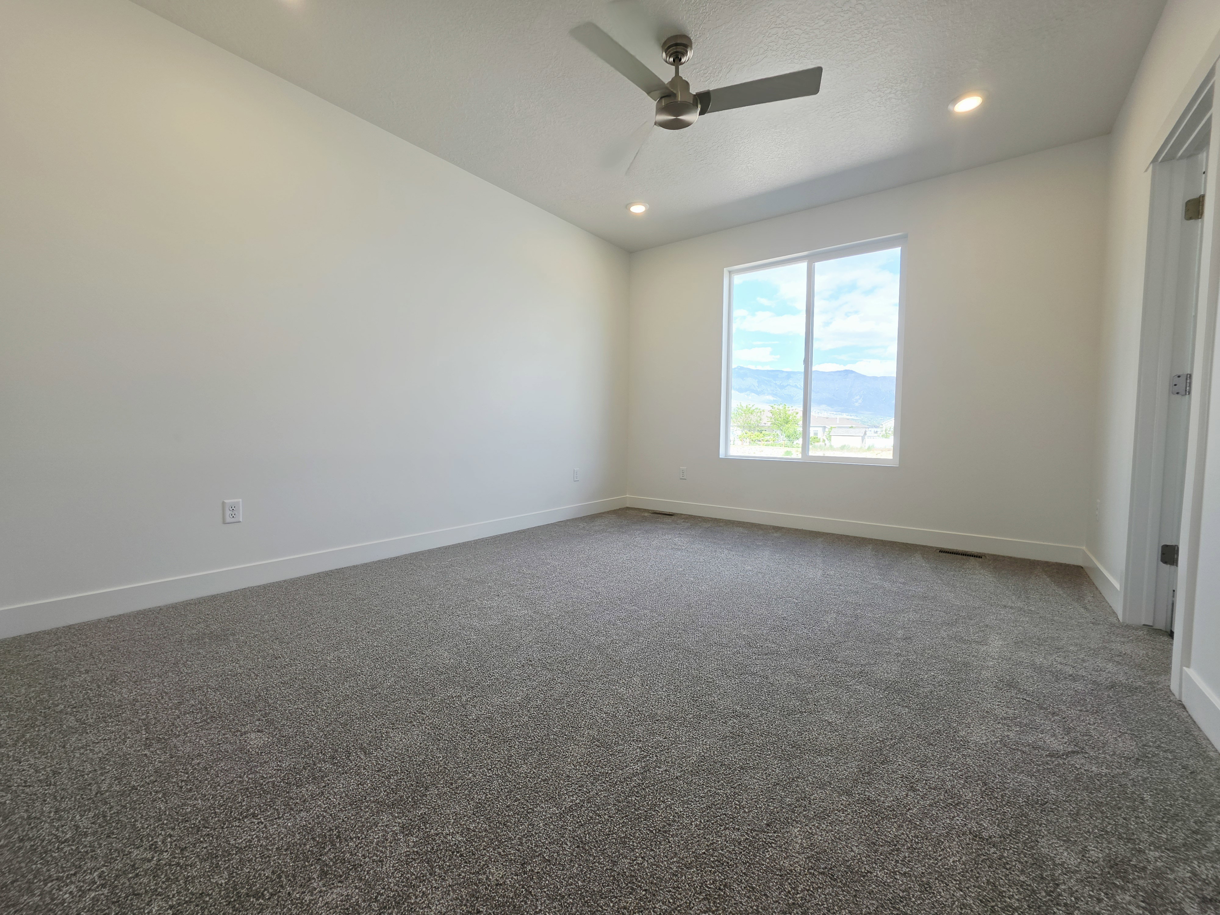Spacious room featuring neutral carpeting, white walls, a large window offering mountain scenery, a ceiling fan, and recessed lighting