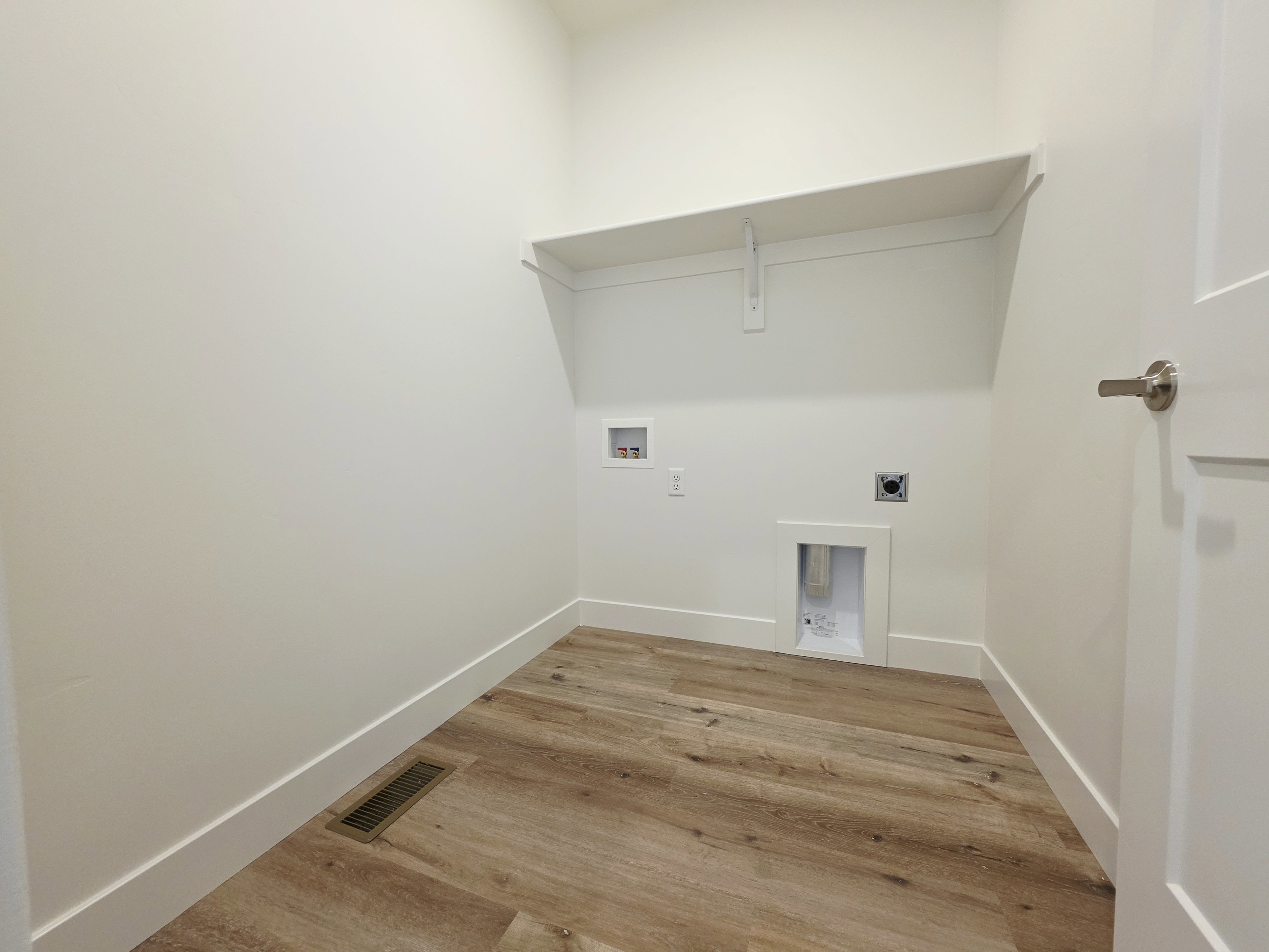 Utility area featuring wood-finish flooring, a wall-mounted shelf, and white baseboards