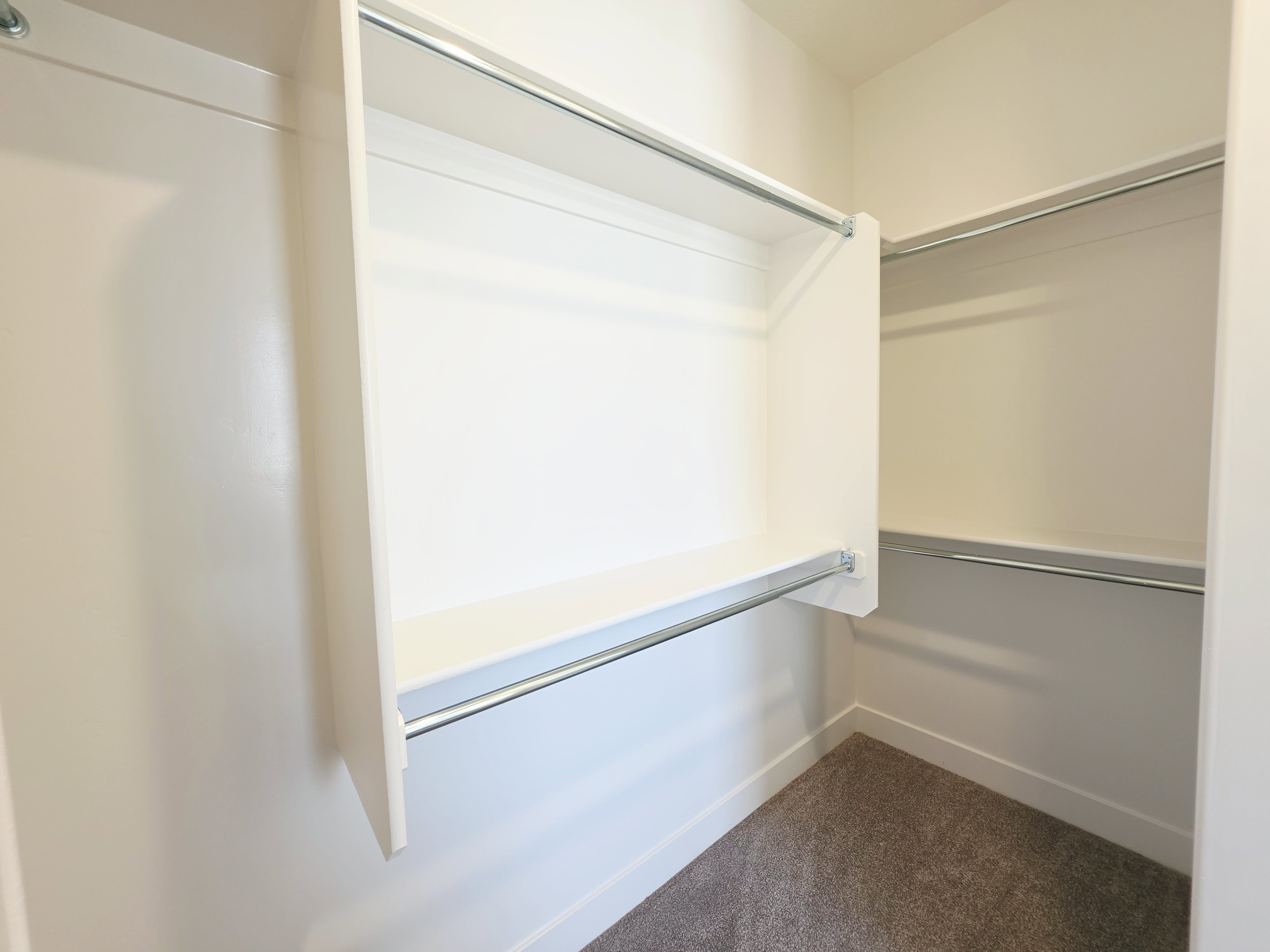 Walk-in closet featuring white built-in shelving, chrome hanging rods, and neutral-toned carpeting