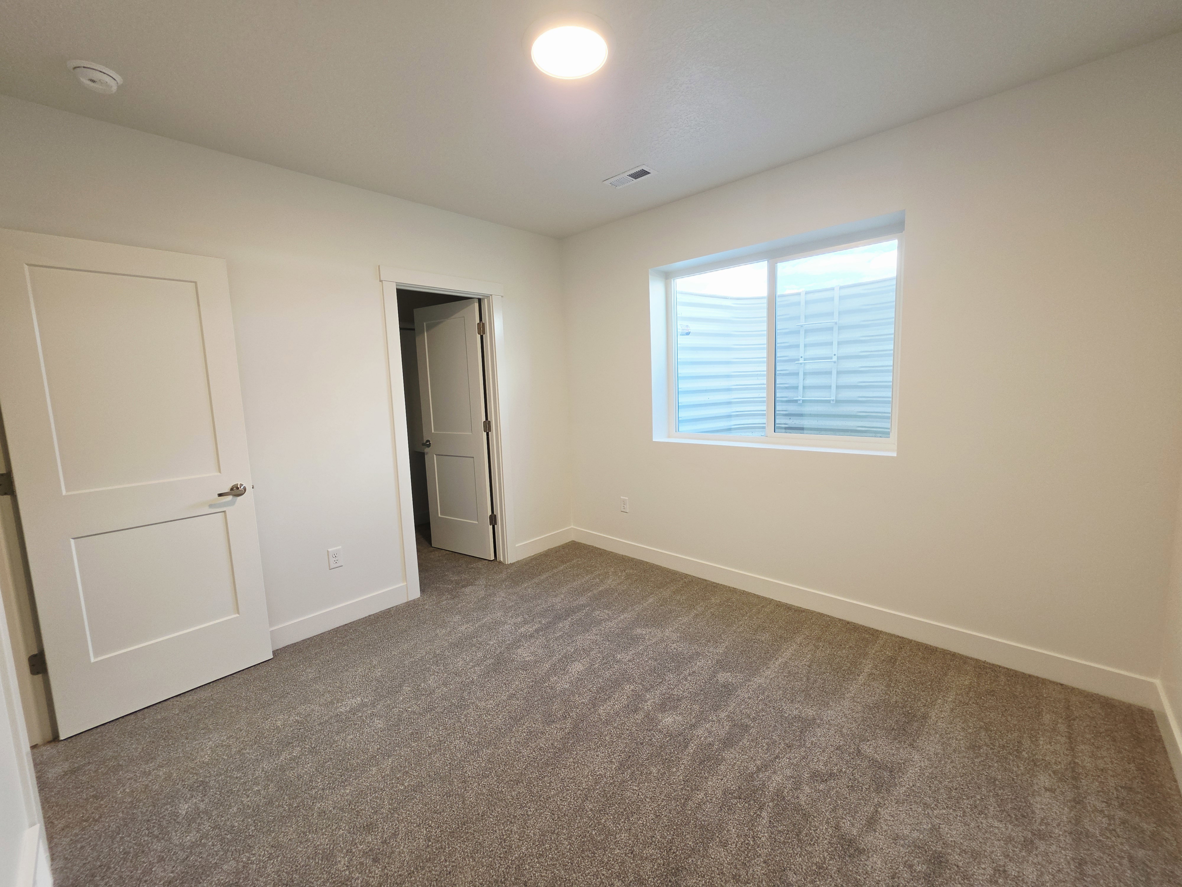 Carpeted room featuring a white interior door with brushed nickel hardware, a white-framed window, recessed lighting, and white baseboards