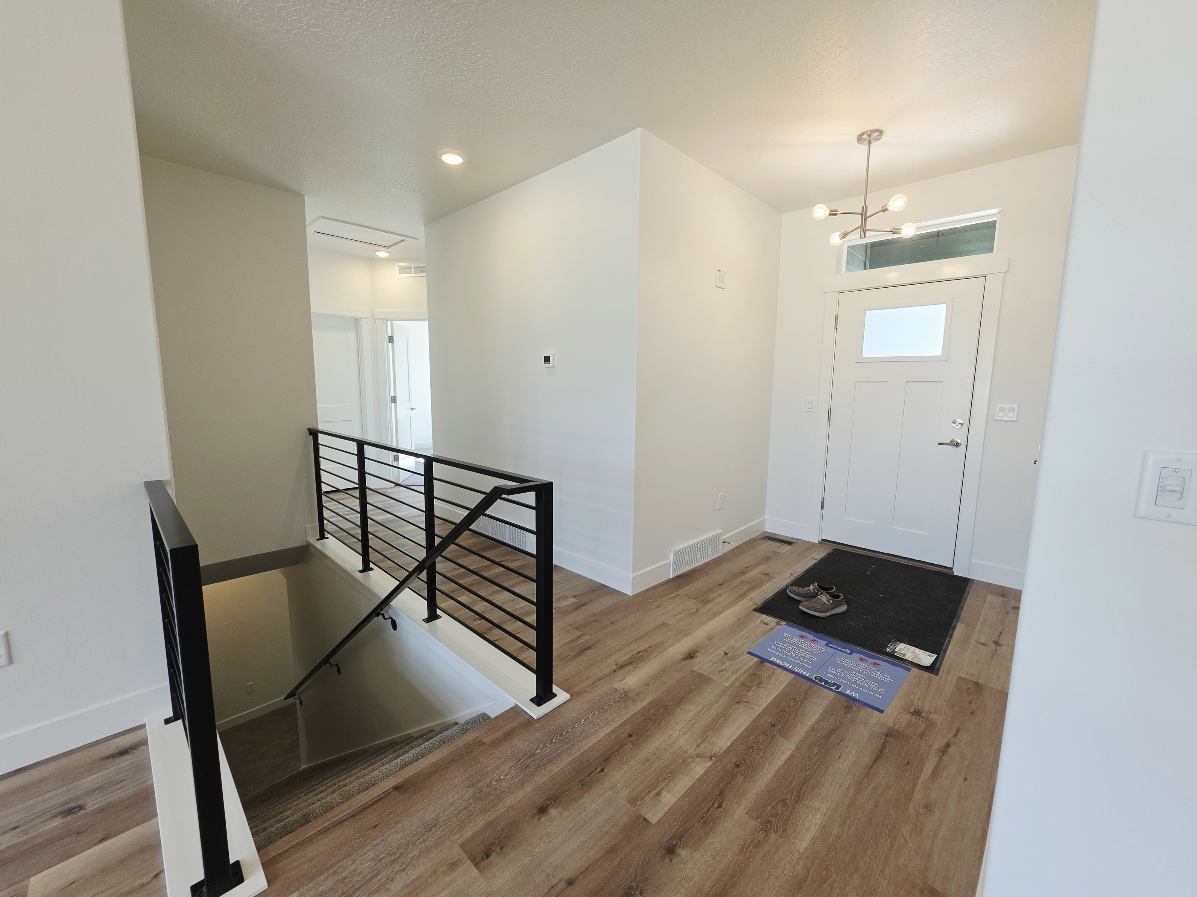 Foyer entry featuring wood-finish flooring, a contemporary chandelier, a white craftsman-style front door with transom window, and a modern horizontal bar railing leading to the lower level