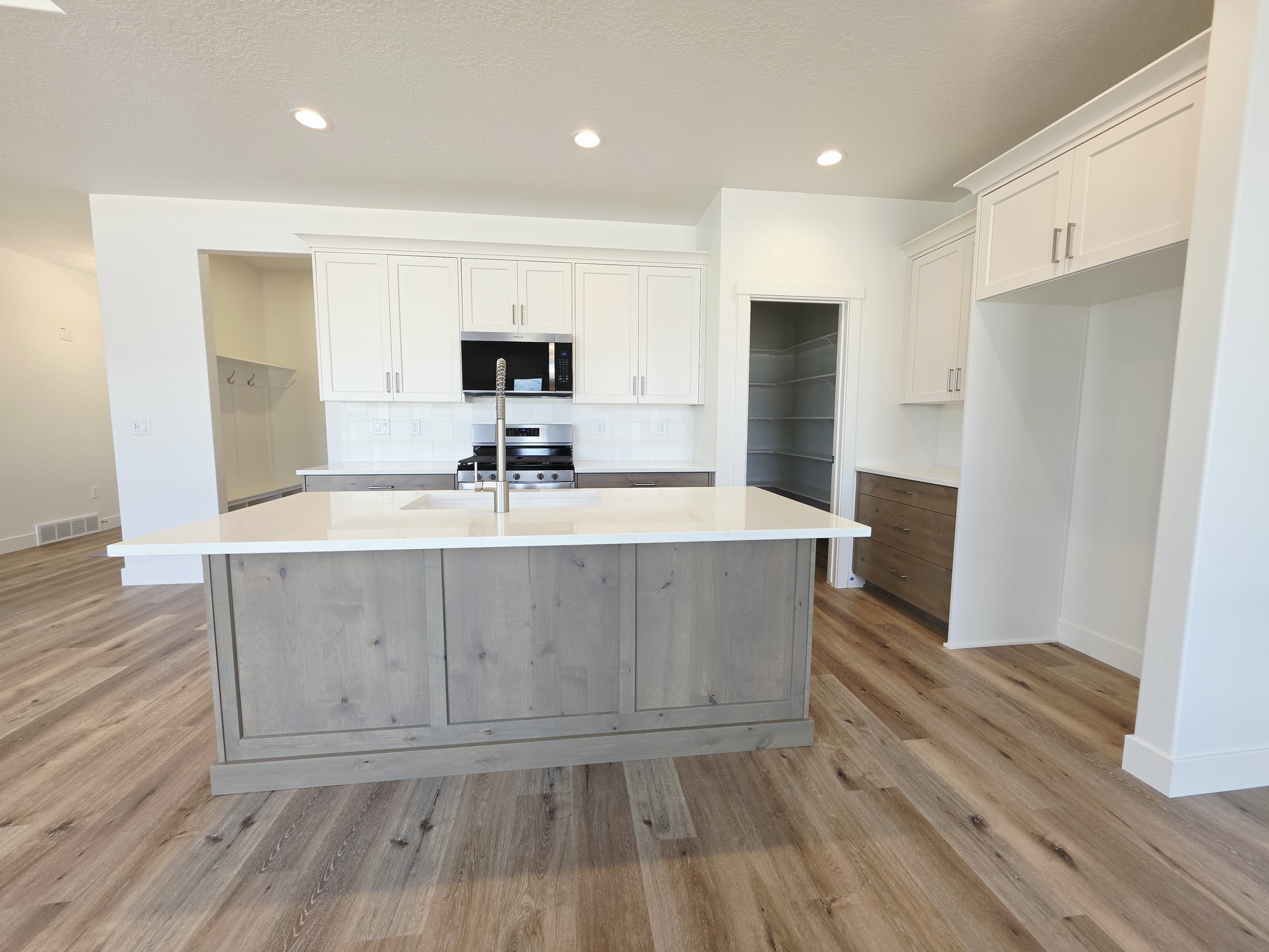 Kitchen featuring a large central island with a built-in sink and stainless steel faucet, wood-finish flooring, white shaker-style cabinetry, and a walk-in pantry