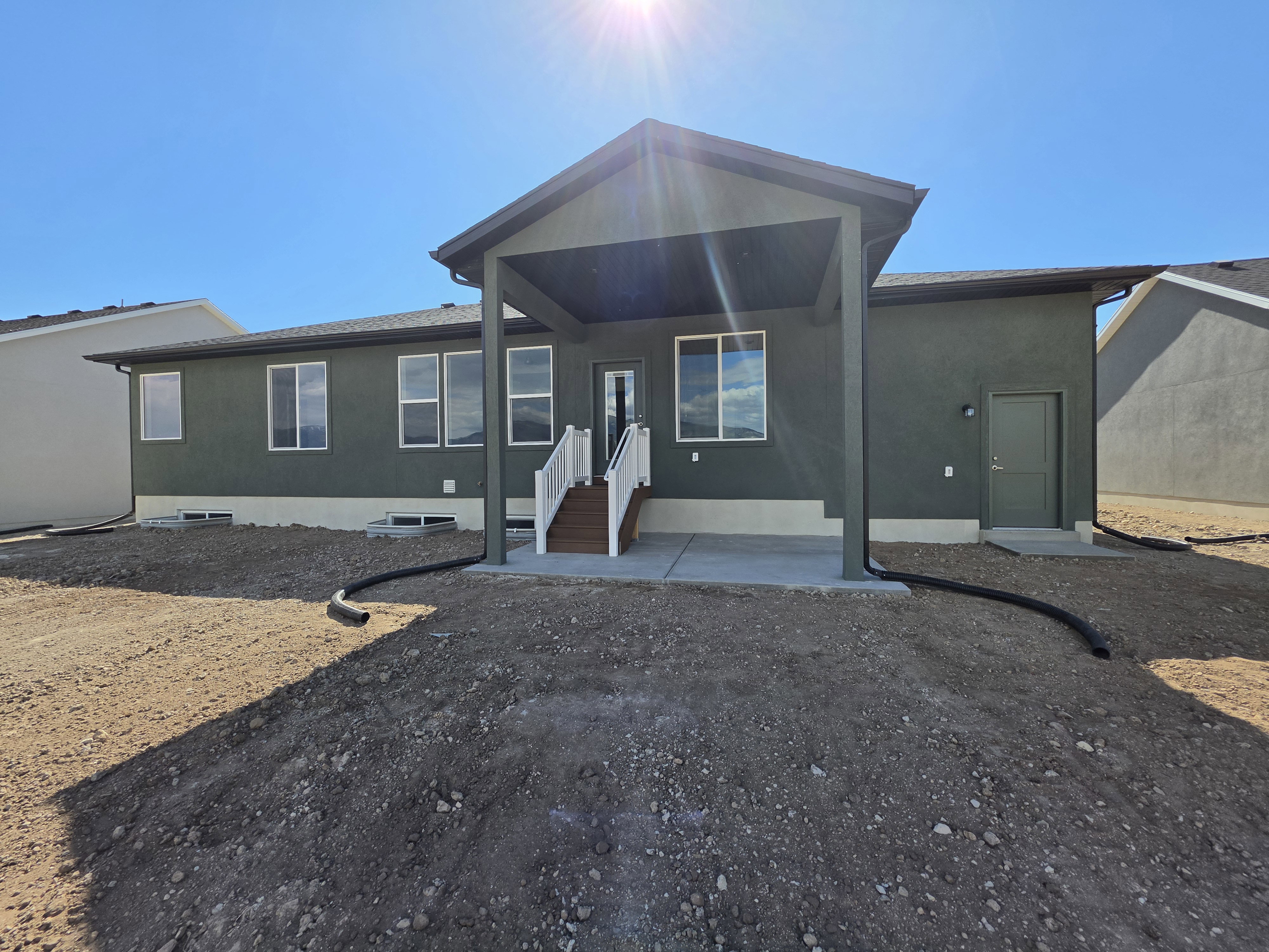 Rear exterior featuring a covered patio with concrete flooring, dark green stucco siding, and a white railing staircase with wood-finish treads
