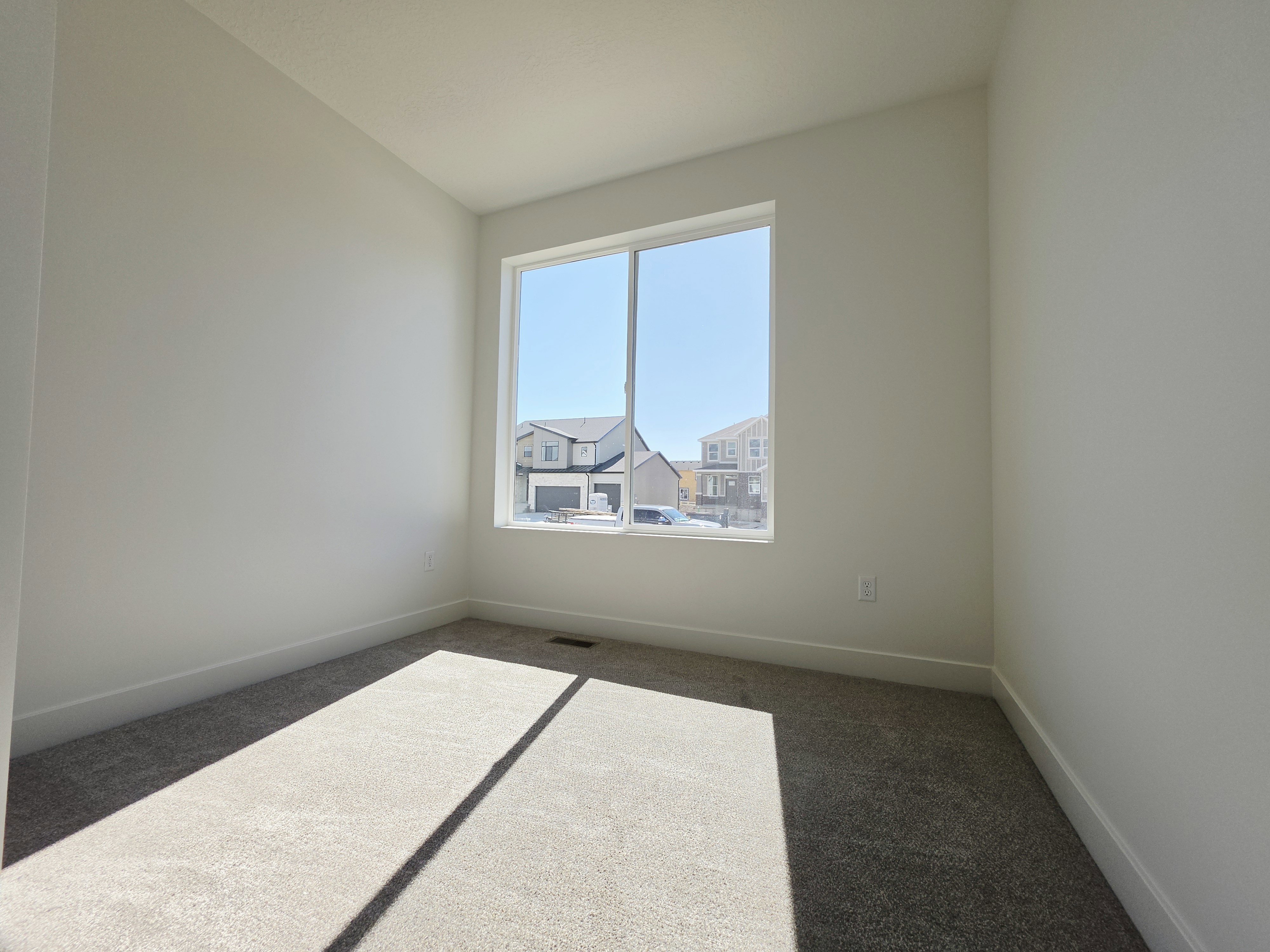 Bright room featuring a large window, neutral wall paint, light-colored carpeting, and white baseboards