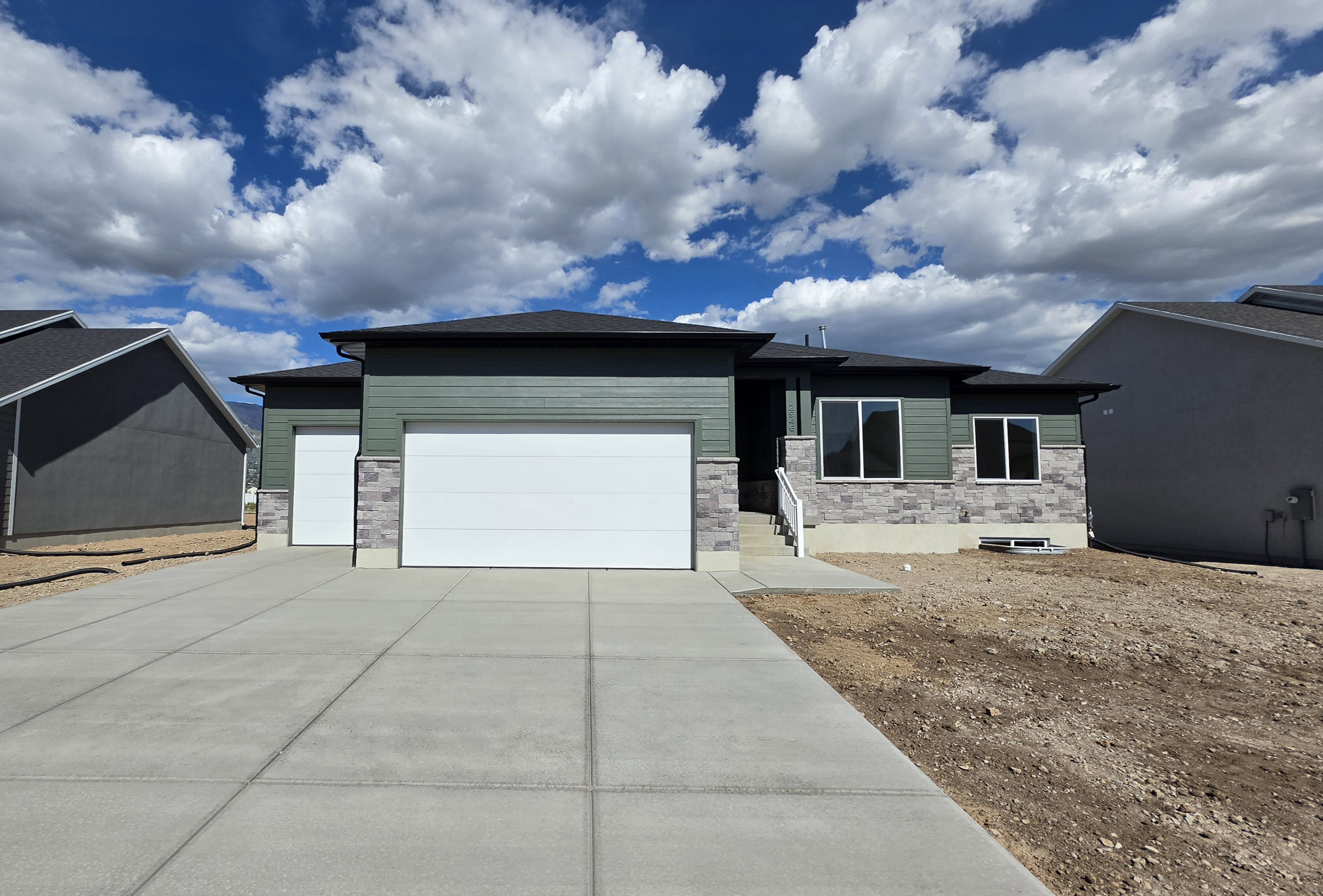 Contemporary single-story residence featuring a two-car garage, an additional single-car garage, green siding, and stone accents