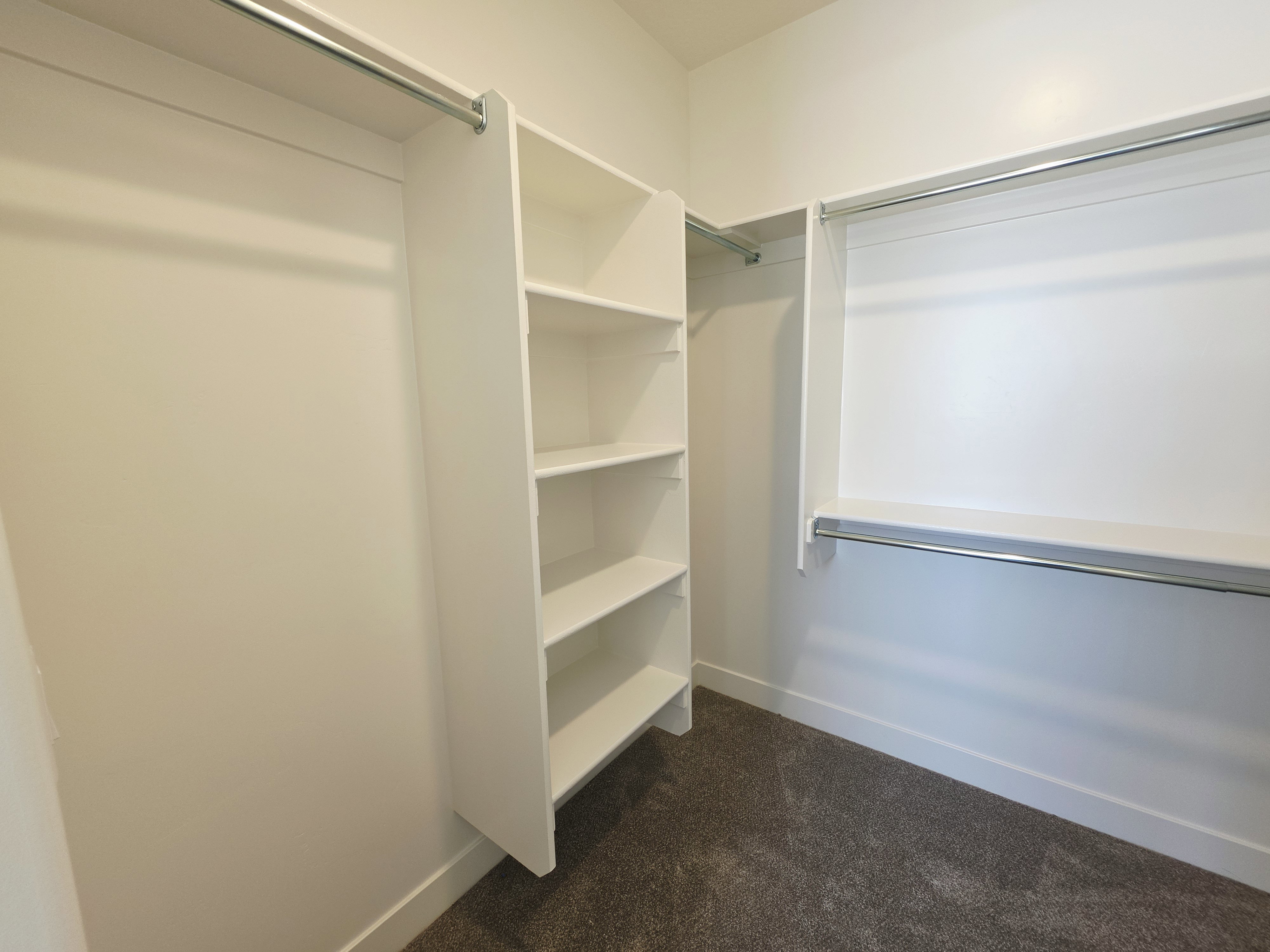 Walk-in closet featuring built-in shelving, multiple hanging rods, white walls, and a grey carpeted floor